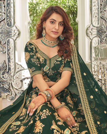 Woman in a green embroidered traditional outfit with jewelry, sitting in front of decorative mirrors.