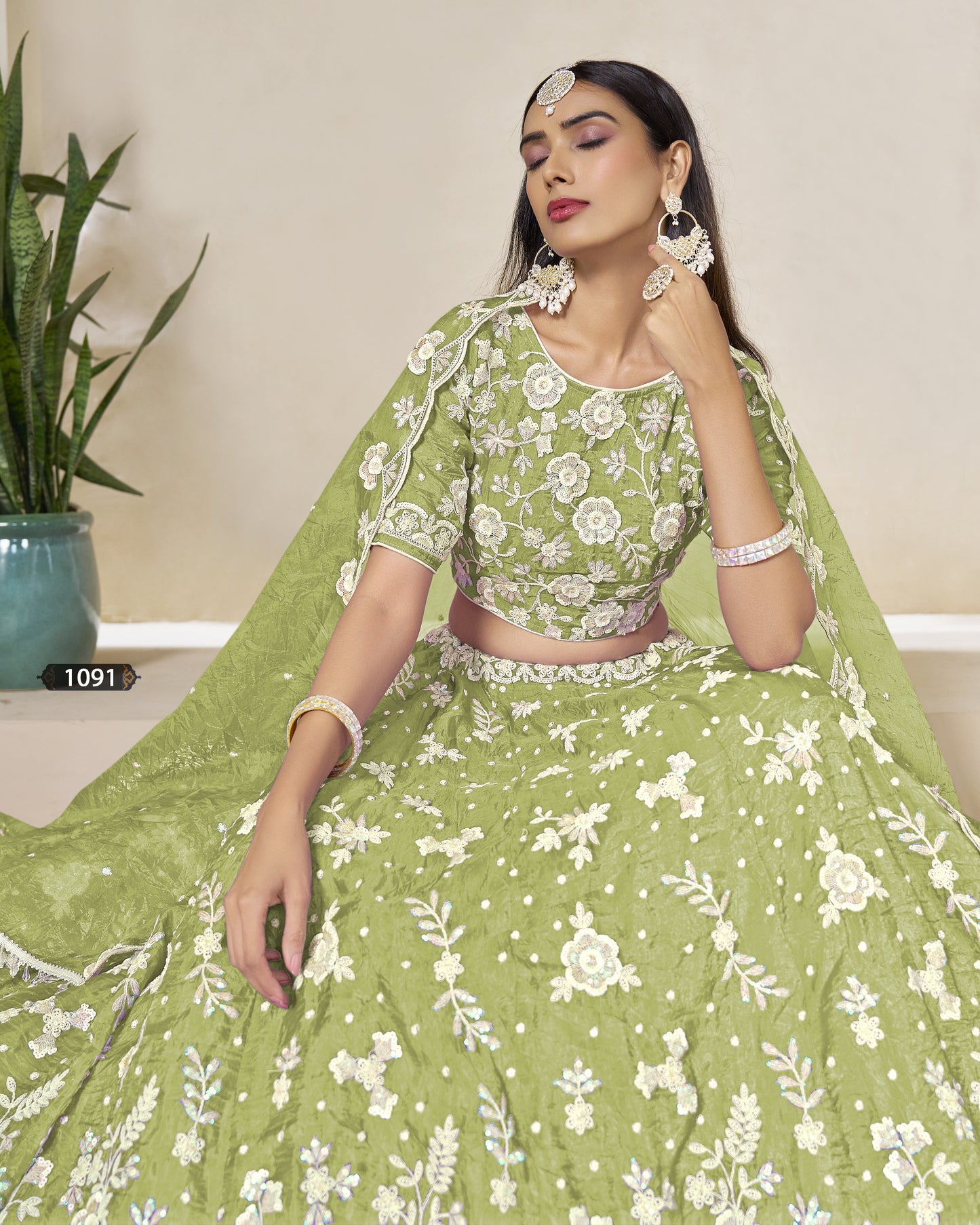 Woman wearing a green traditional outfit with white floral patterns, sitting indoors.