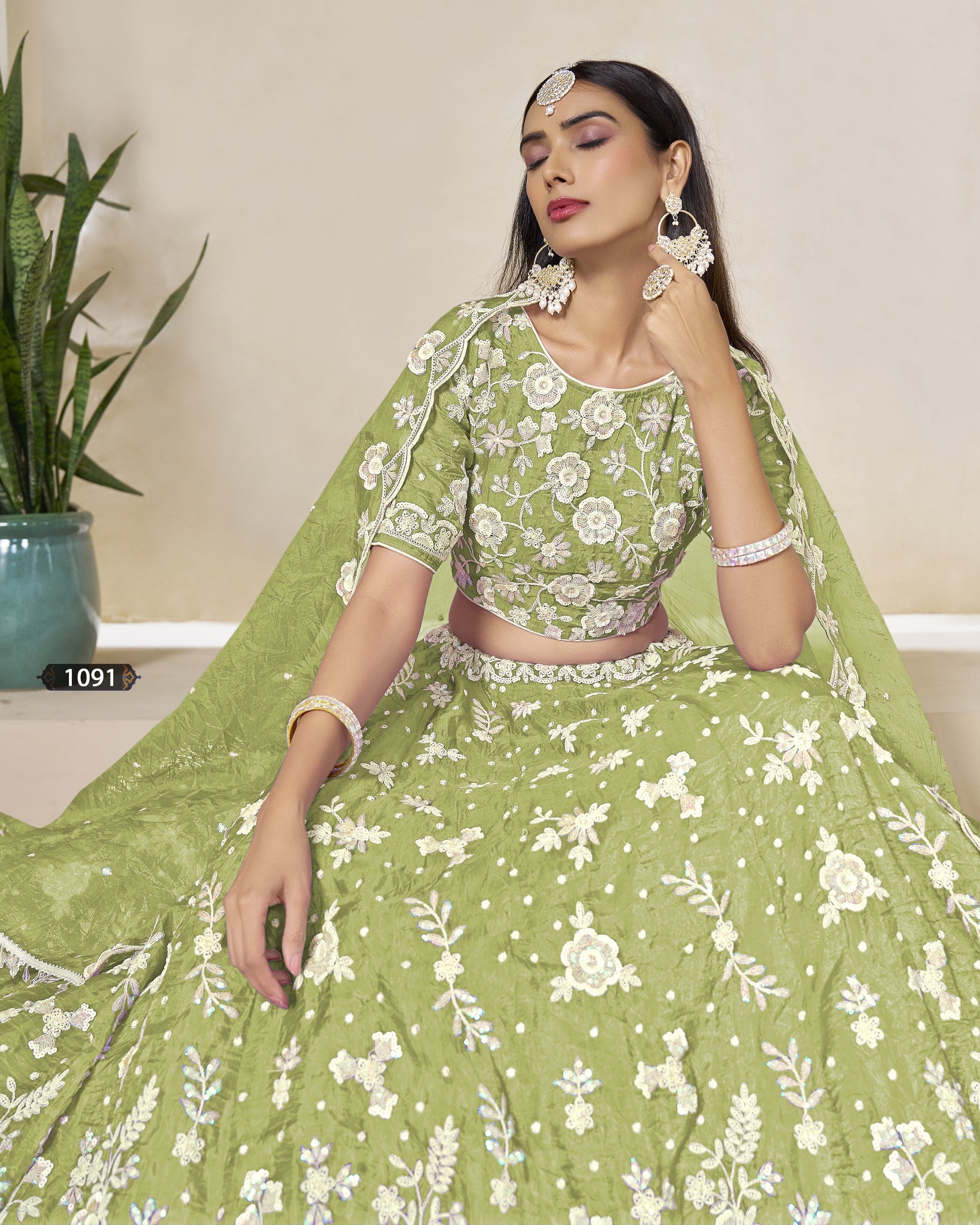 Woman wearing a green traditional outfit with white floral patterns, sitting indoors.