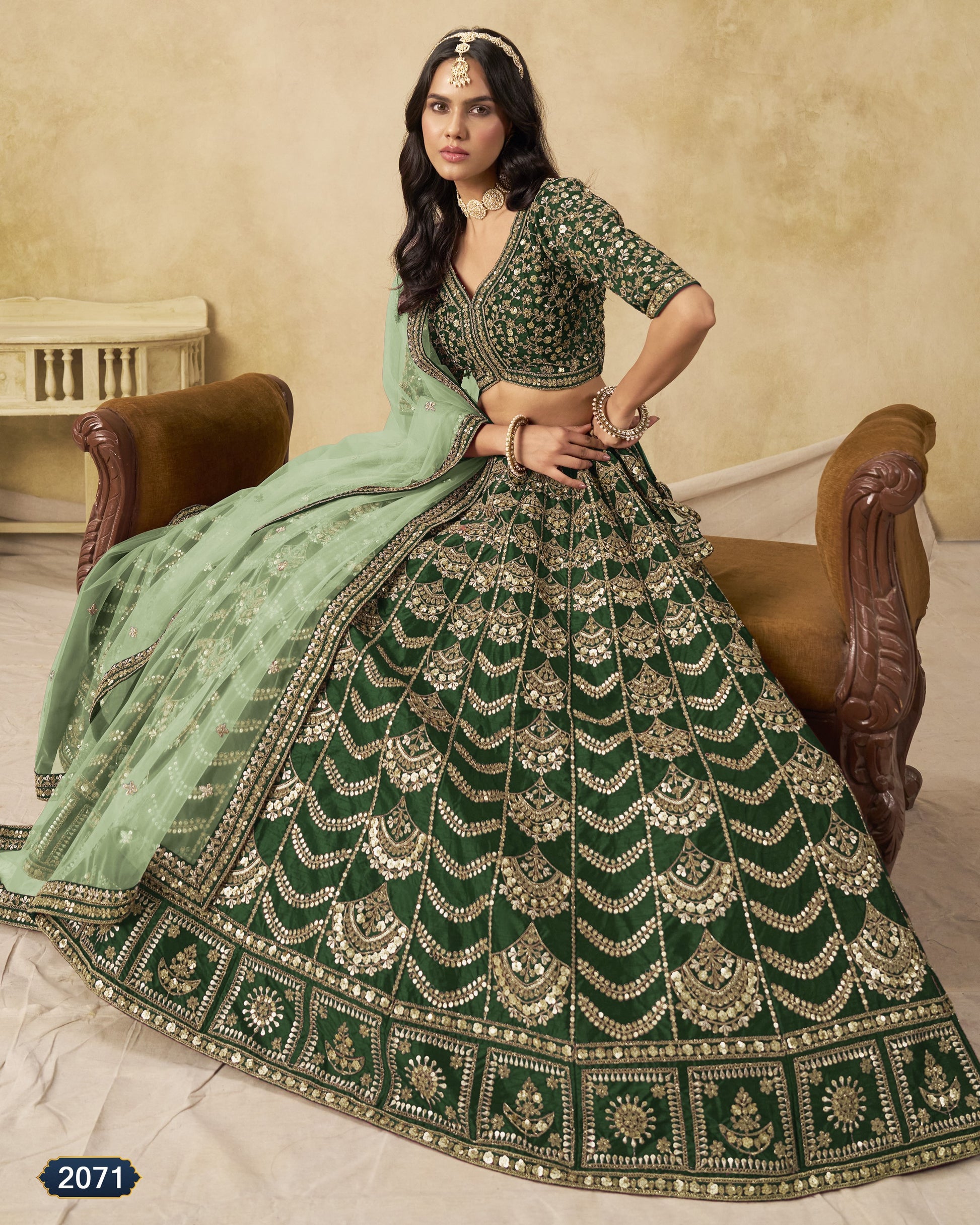 Woman wearing a green and gold embroidered traditional outfit sitting on a wooden chair.