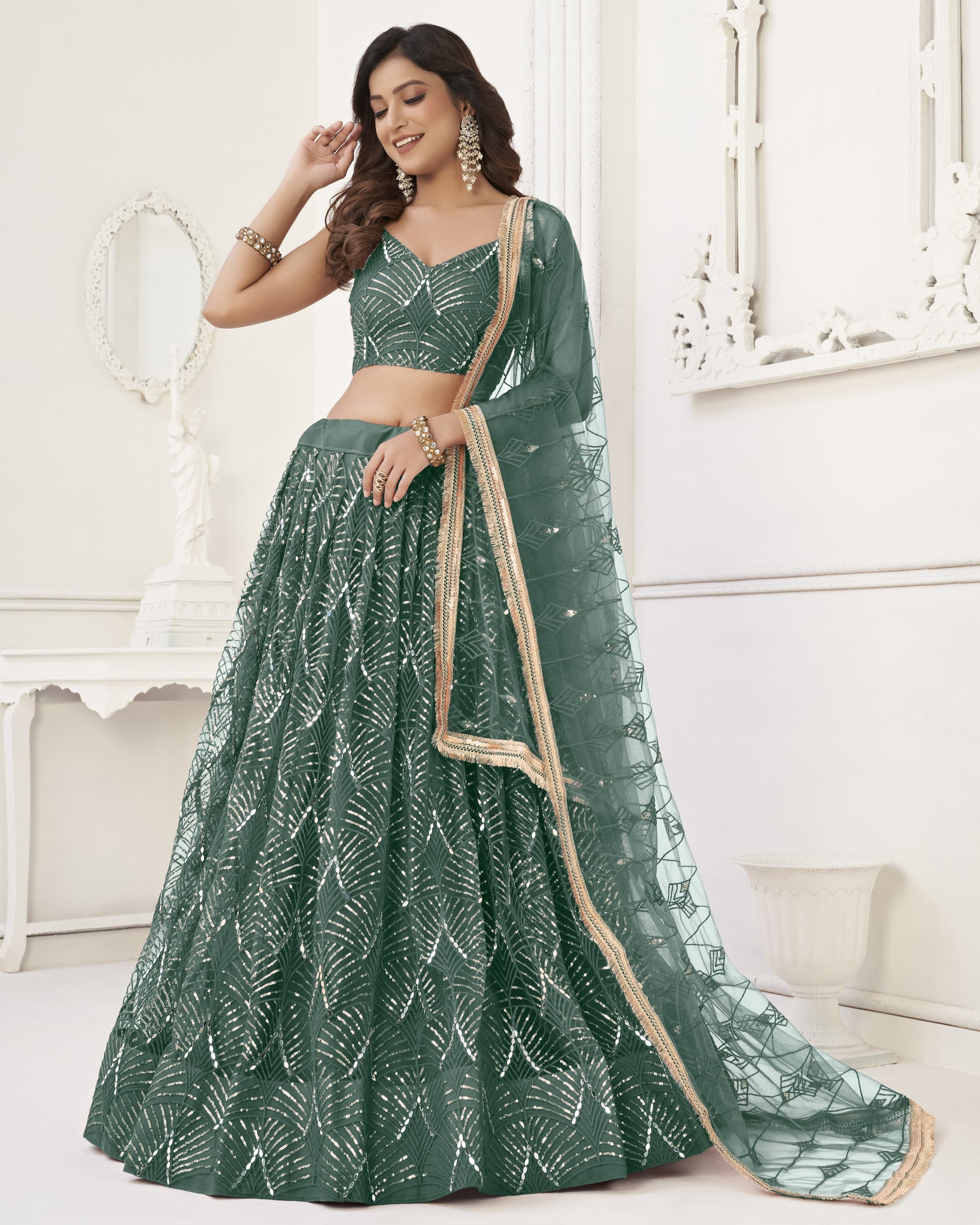 Woman wearing a green traditional outfit with a white pattern in a white room.