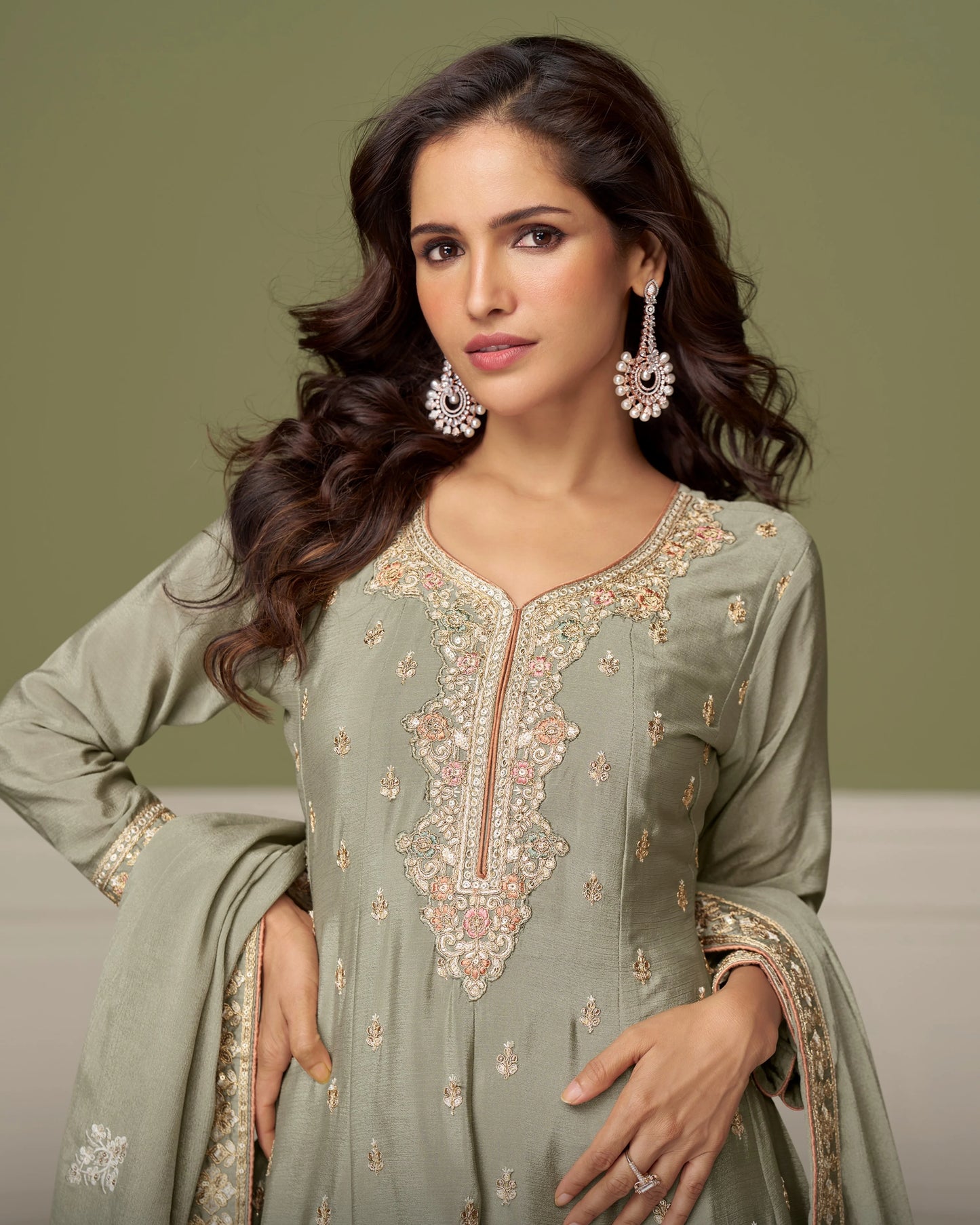 Woman wearing a light green embroidered traditional outfit with a neutral background