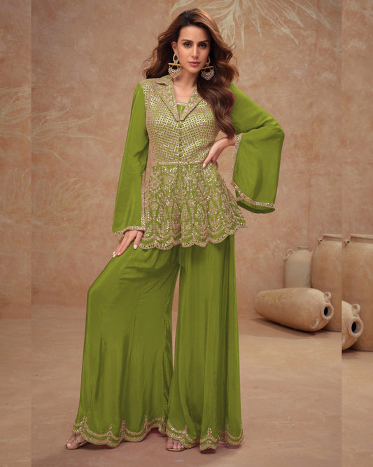 Woman wearing a green traditional outfit with intricate patterns in a beige room.