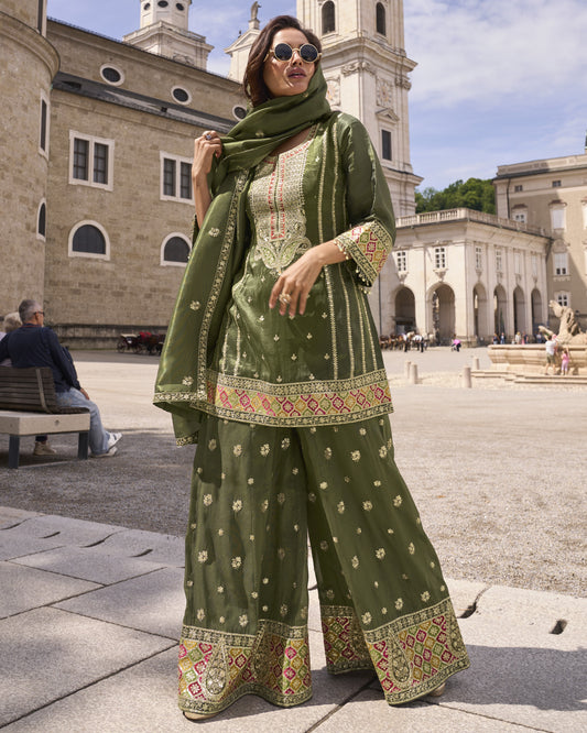 Woman in traditional green outfit with embroidery standing in an outdoor setting with historical architecture.