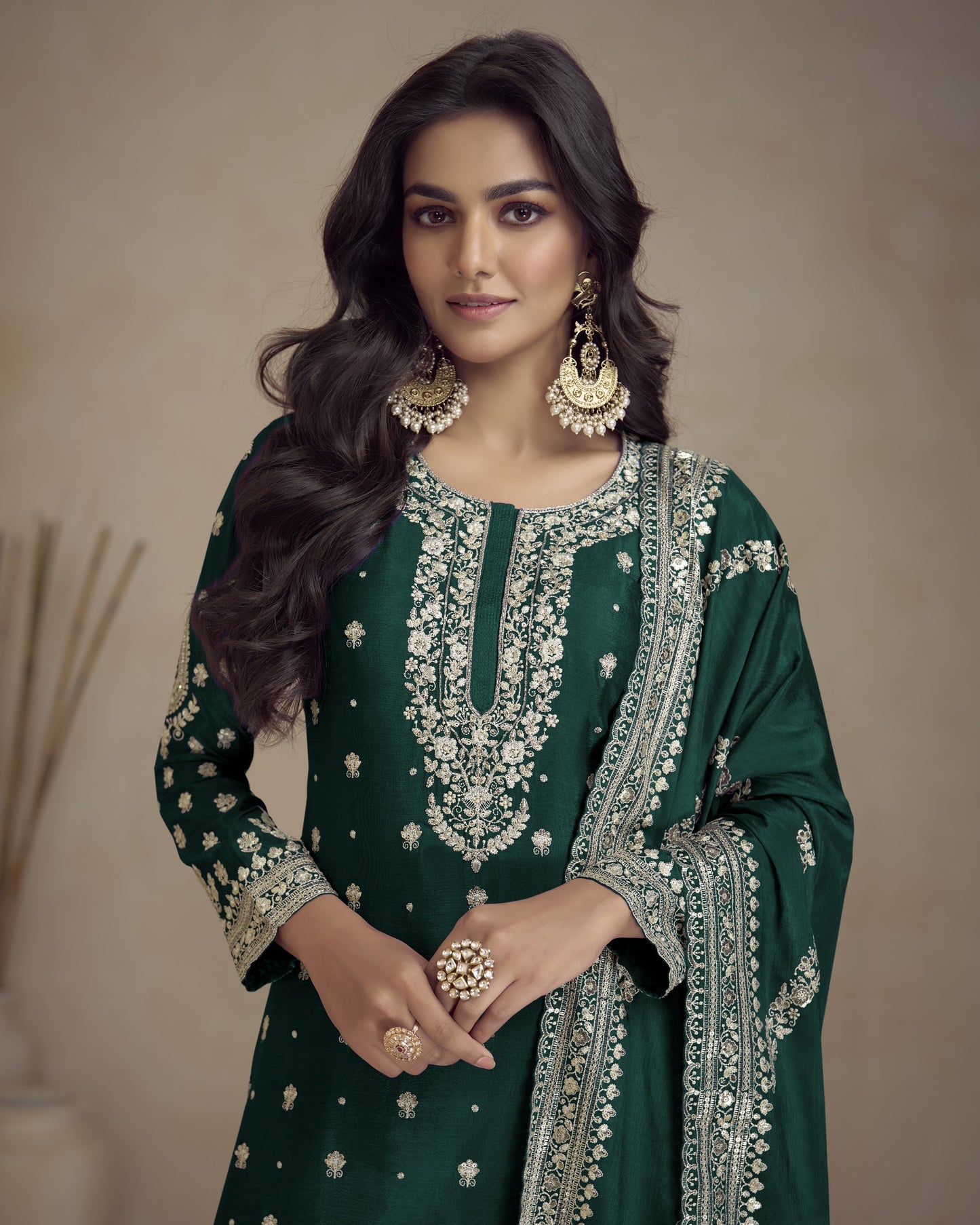 Woman wearing a green embroidered traditional outfit with gold details on a beige background