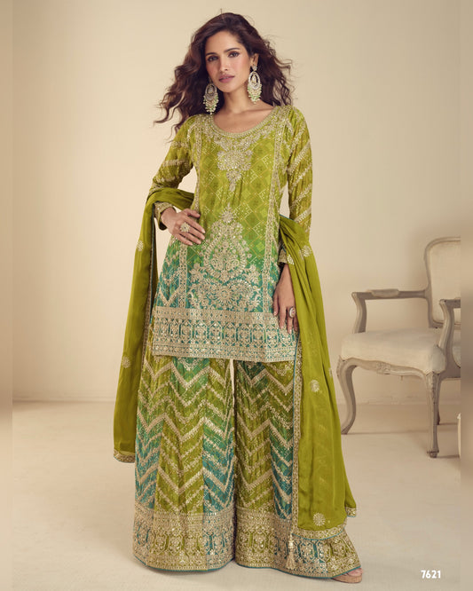 Woman wearing a green embroidered traditional outfit with a matching dupatta in a room.