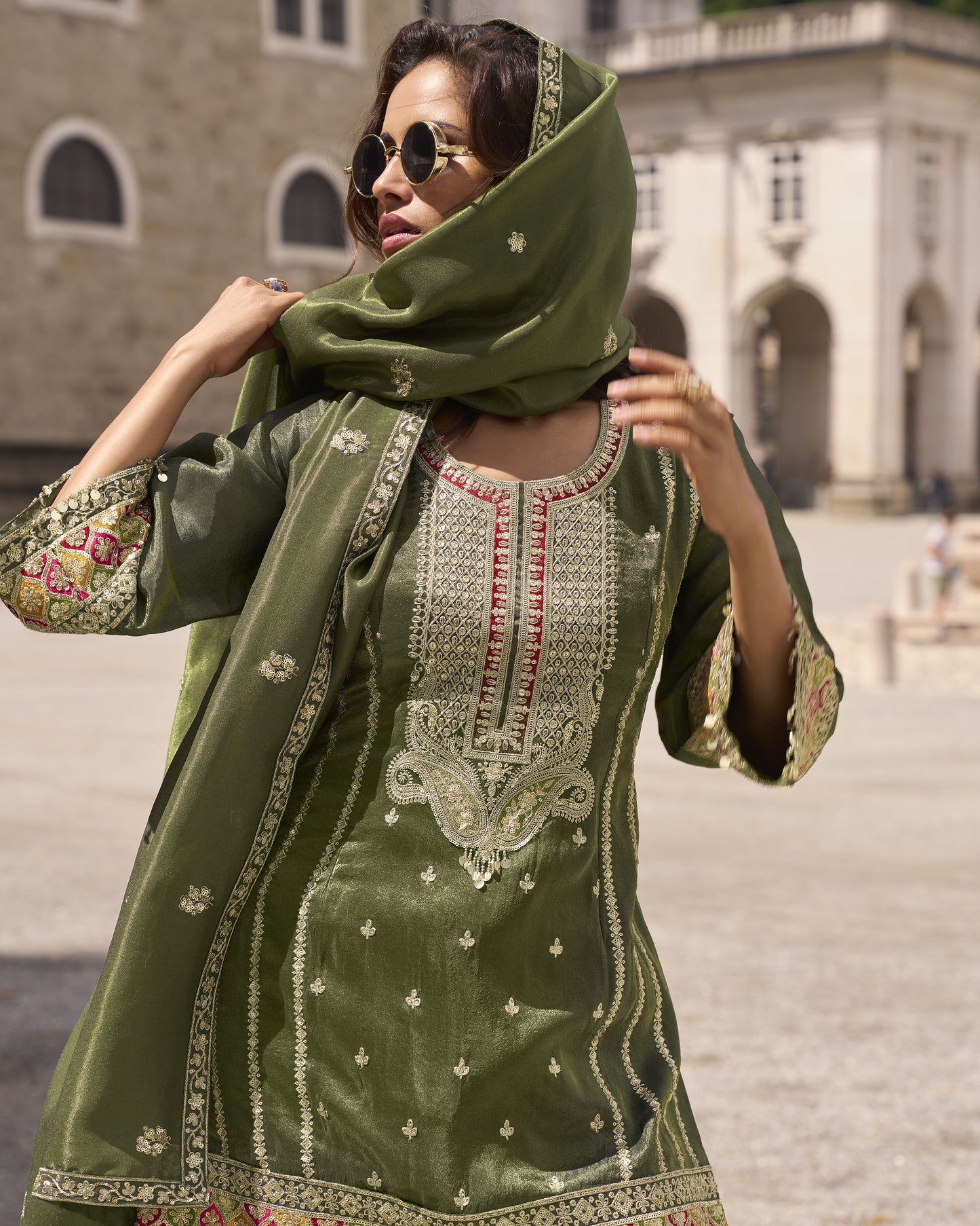 Woman wearing a green embroidered traditional outfit with a matching scarf in an outdoor setting.