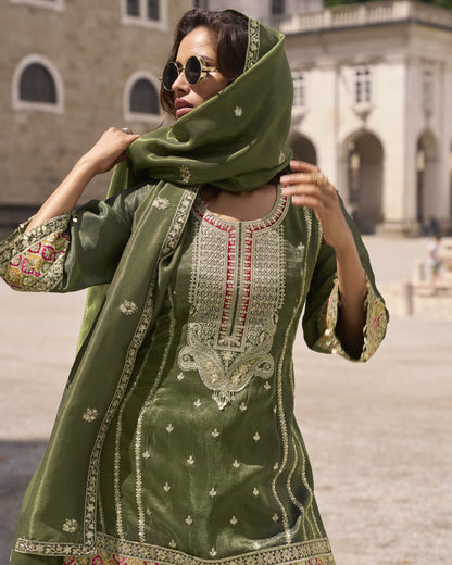Woman wearing a green embroidered traditional outfit with a matching scarf in an outdoor setting.