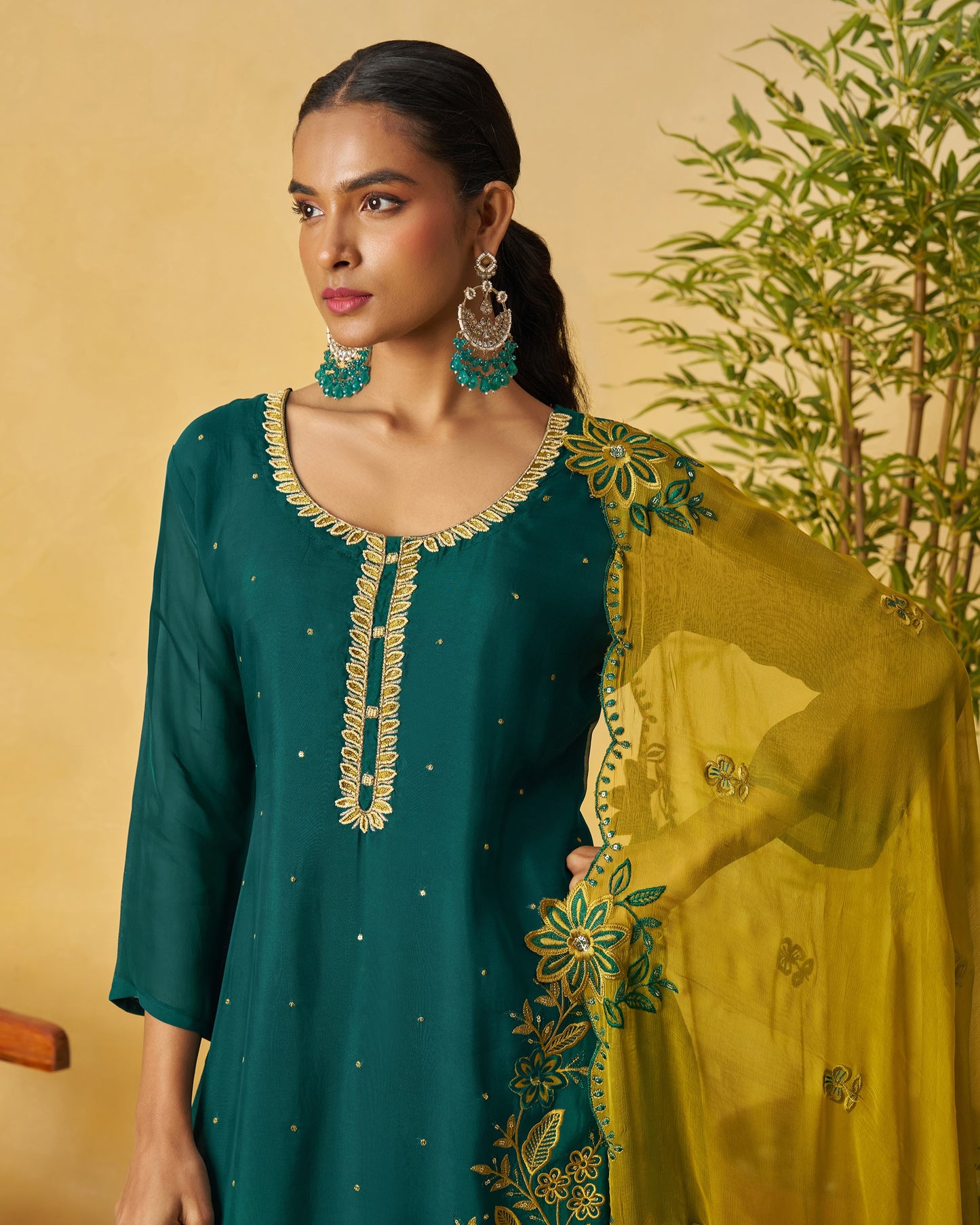 Woman wearing a green and yellow embroidered outfit with a beige background