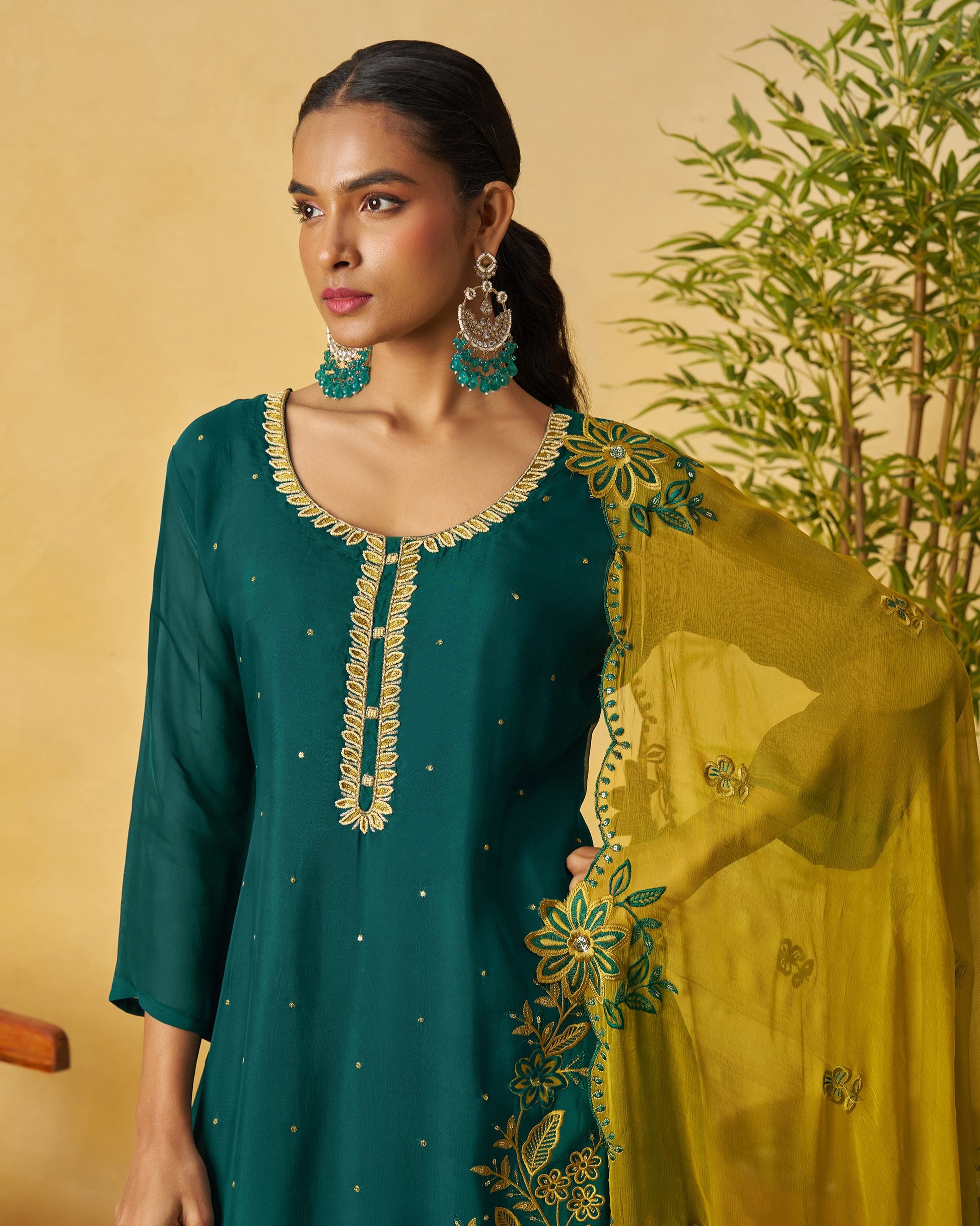 Woman wearing a green and yellow embroidered outfit with a beige background