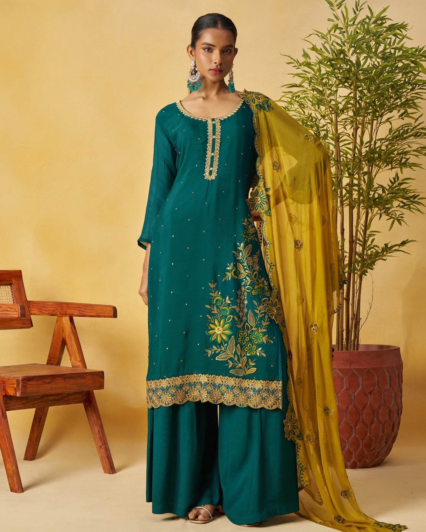 Woman in teal traditional outfit with yellow dupatta against a beige background