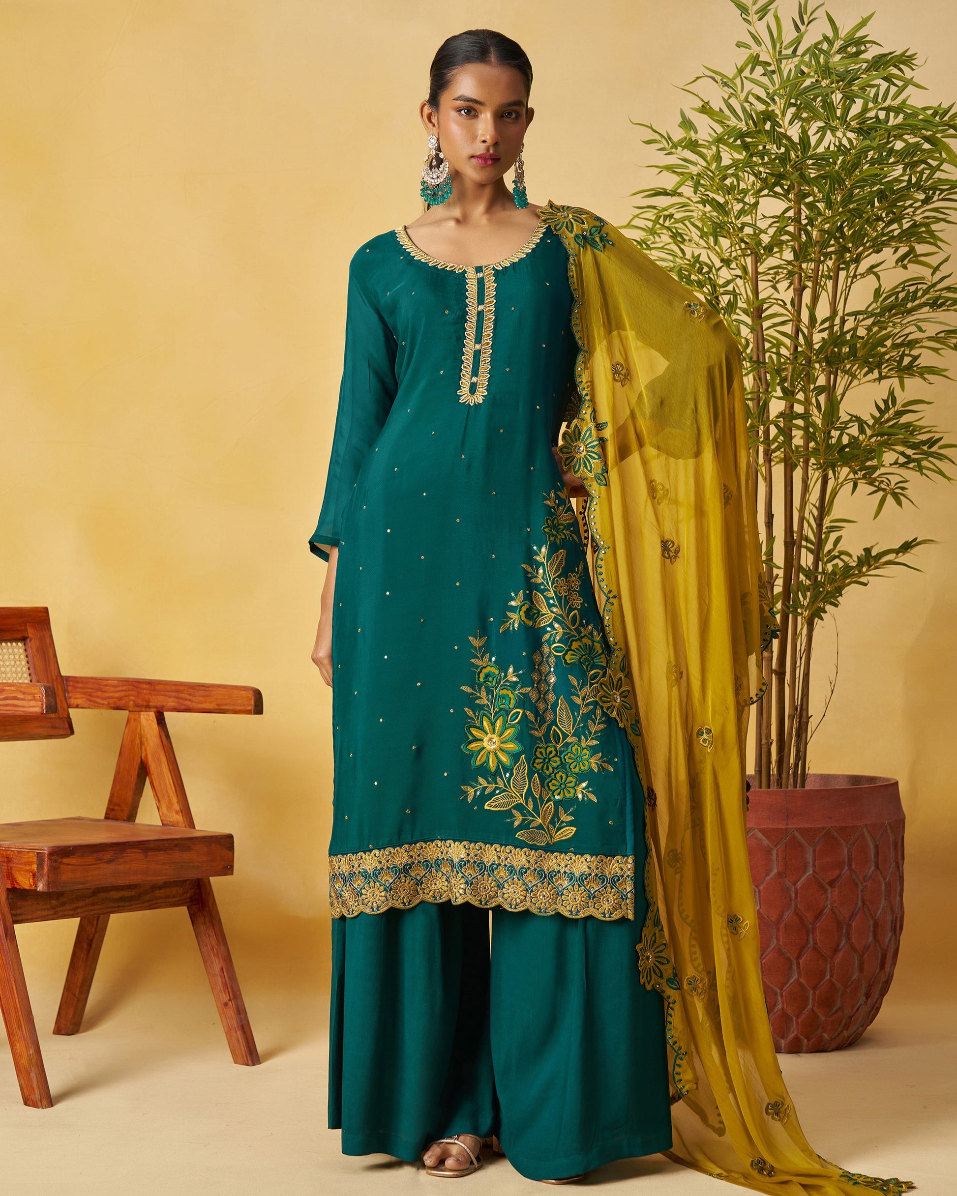 Woman in teal traditional outfit with yellow dupatta against a beige background