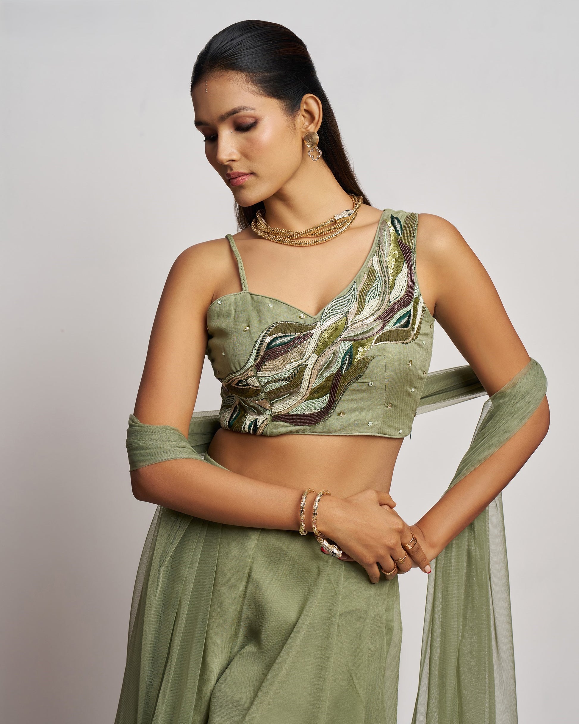 Woman wearing a green traditional outfit with intricate detailing on a plain background