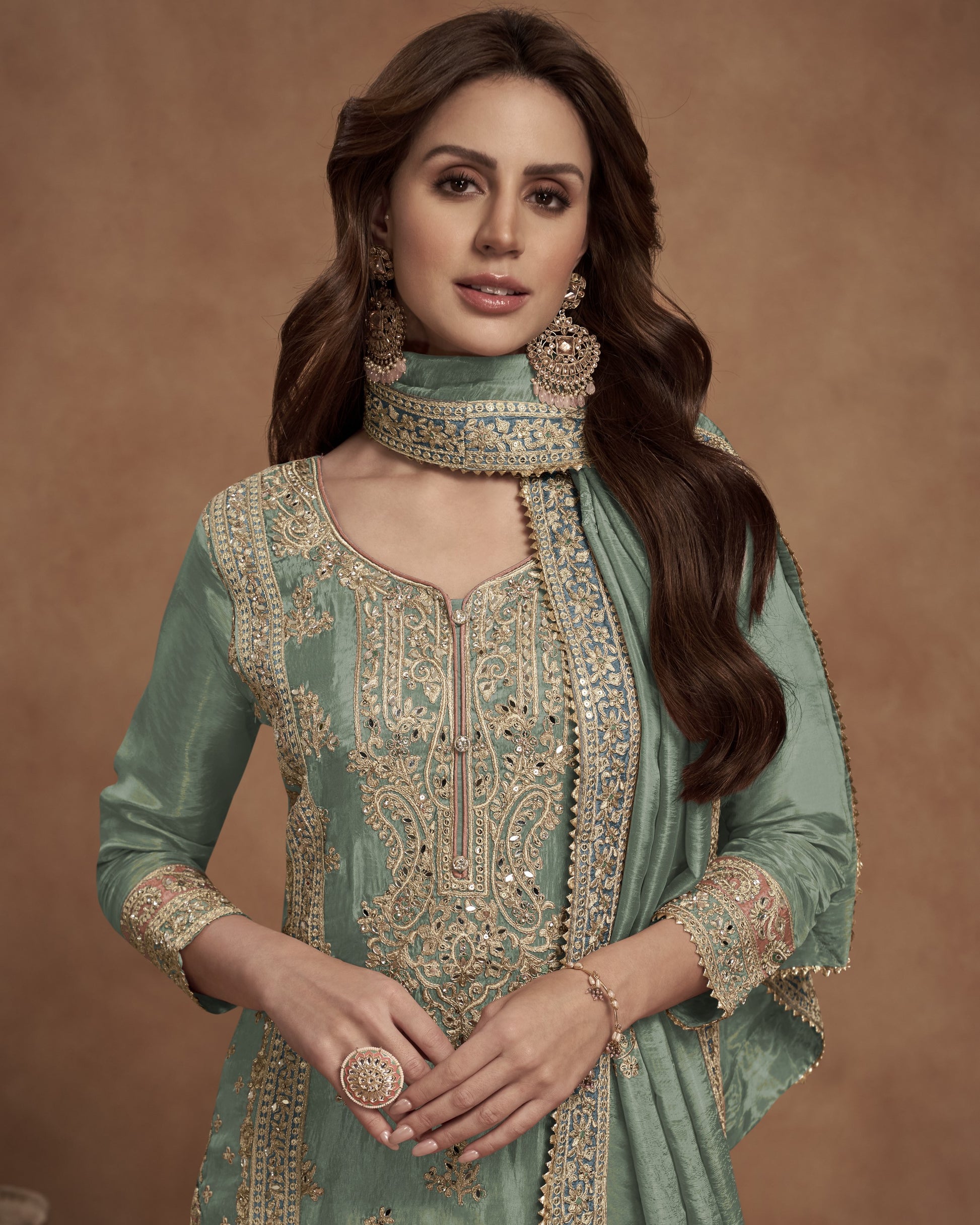 Woman wearing a traditional green embroidered outfit with jewelry against a brown background