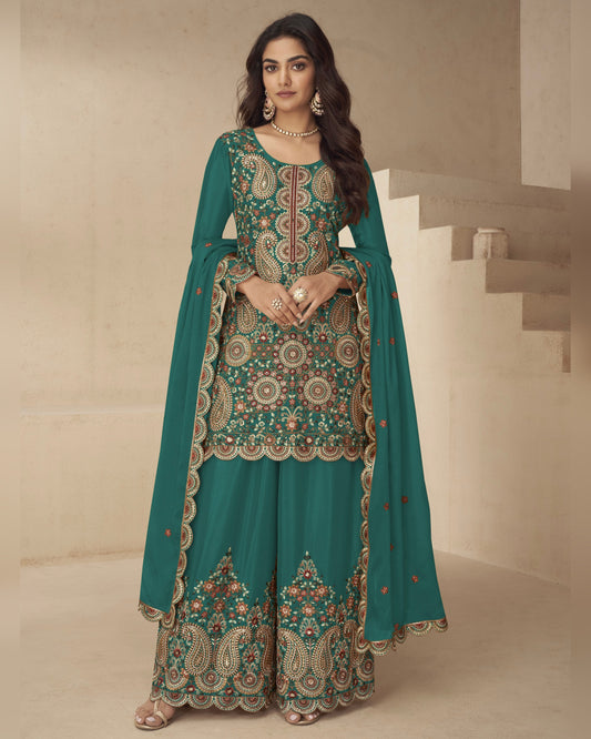 Woman wearing a teal embroidered traditional outfit in a neutral setting