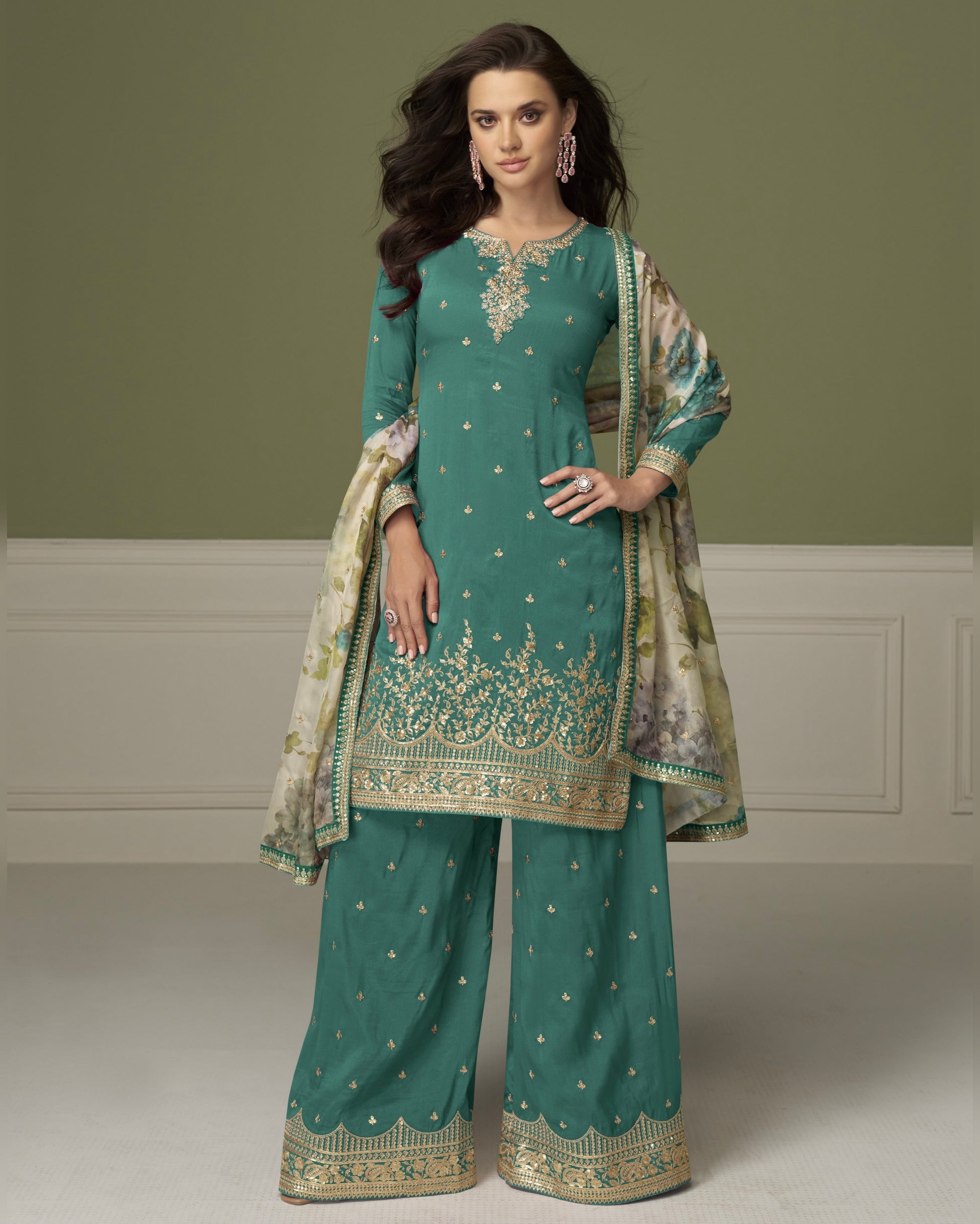 Woman wearing a teal embroidered traditional outfit with a matching dupatta on a plain background