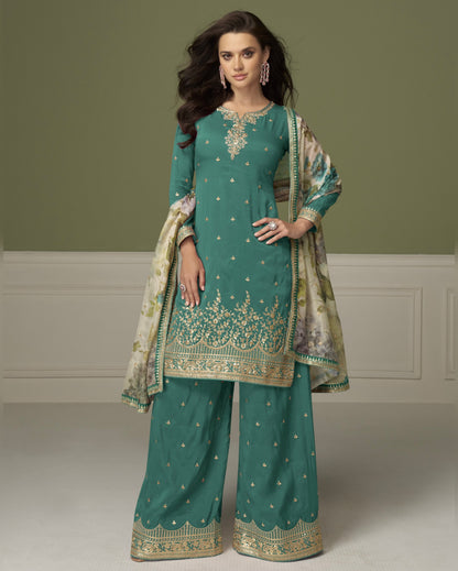 Woman wearing a teal embroidered traditional outfit with a matching dupatta on a plain background