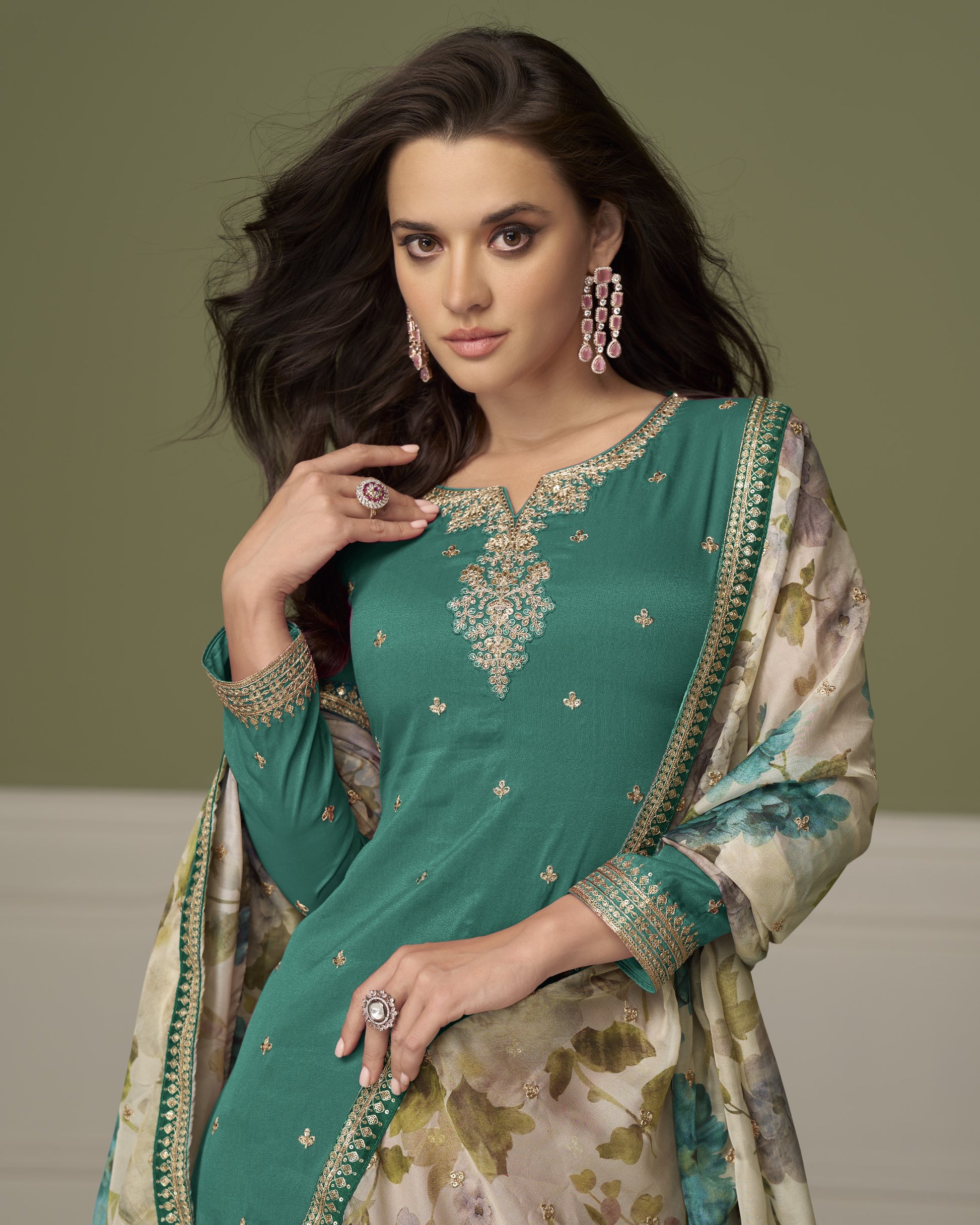 Woman wearing a green embroidered traditional outfit with a floral patterned dupatta against a neutral background