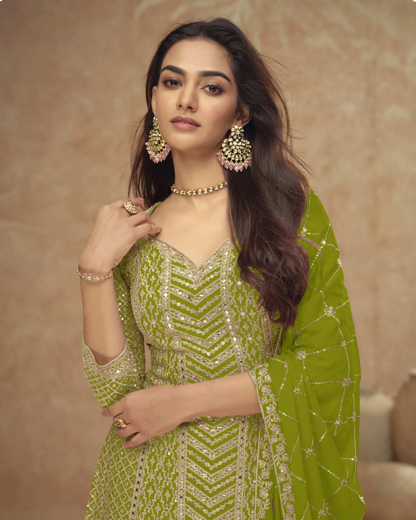 Woman wearing a green traditional outfit with gold jewelry against a beige background
