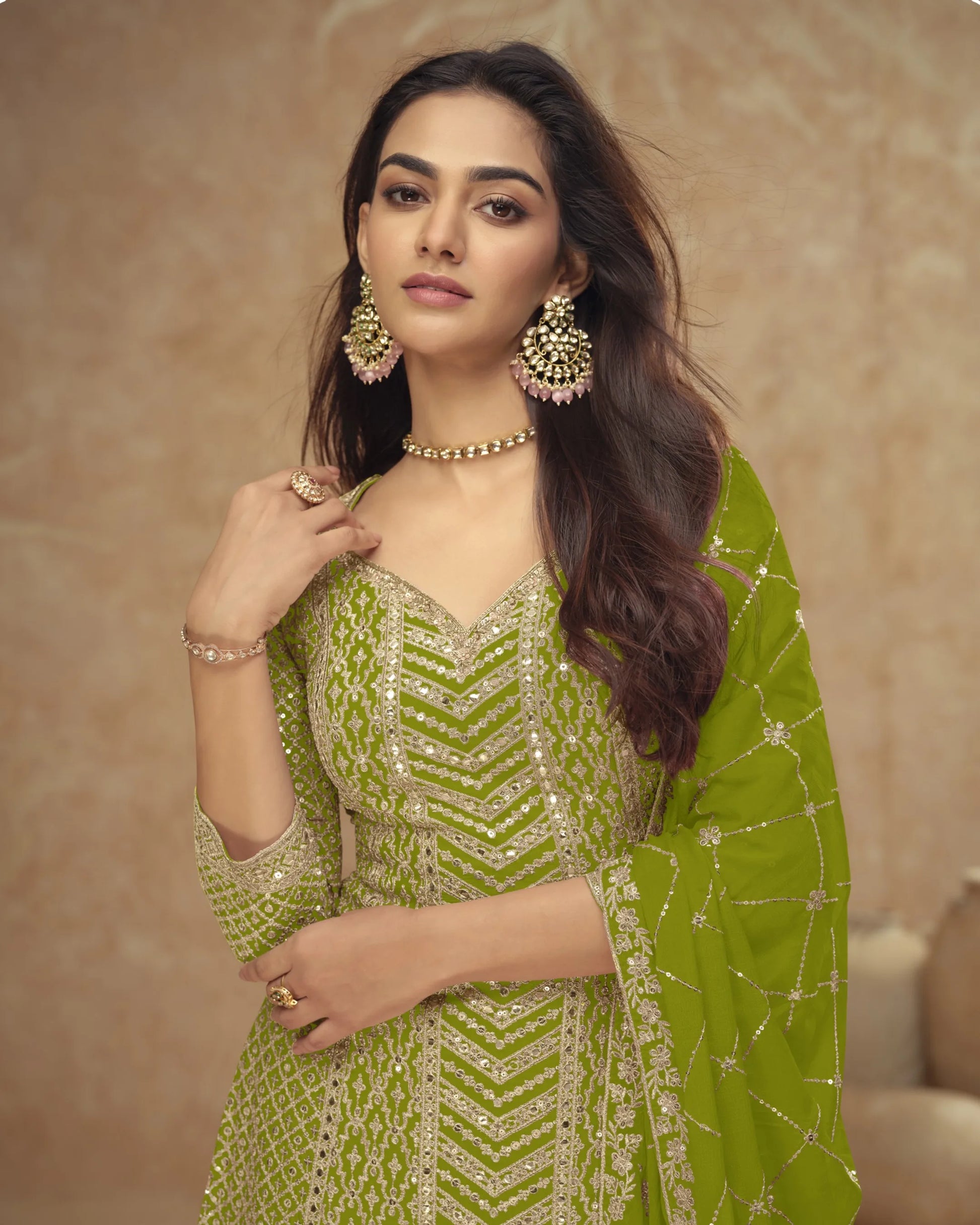 Woman wearing a green traditional outfit with gold jewelry against a beige background