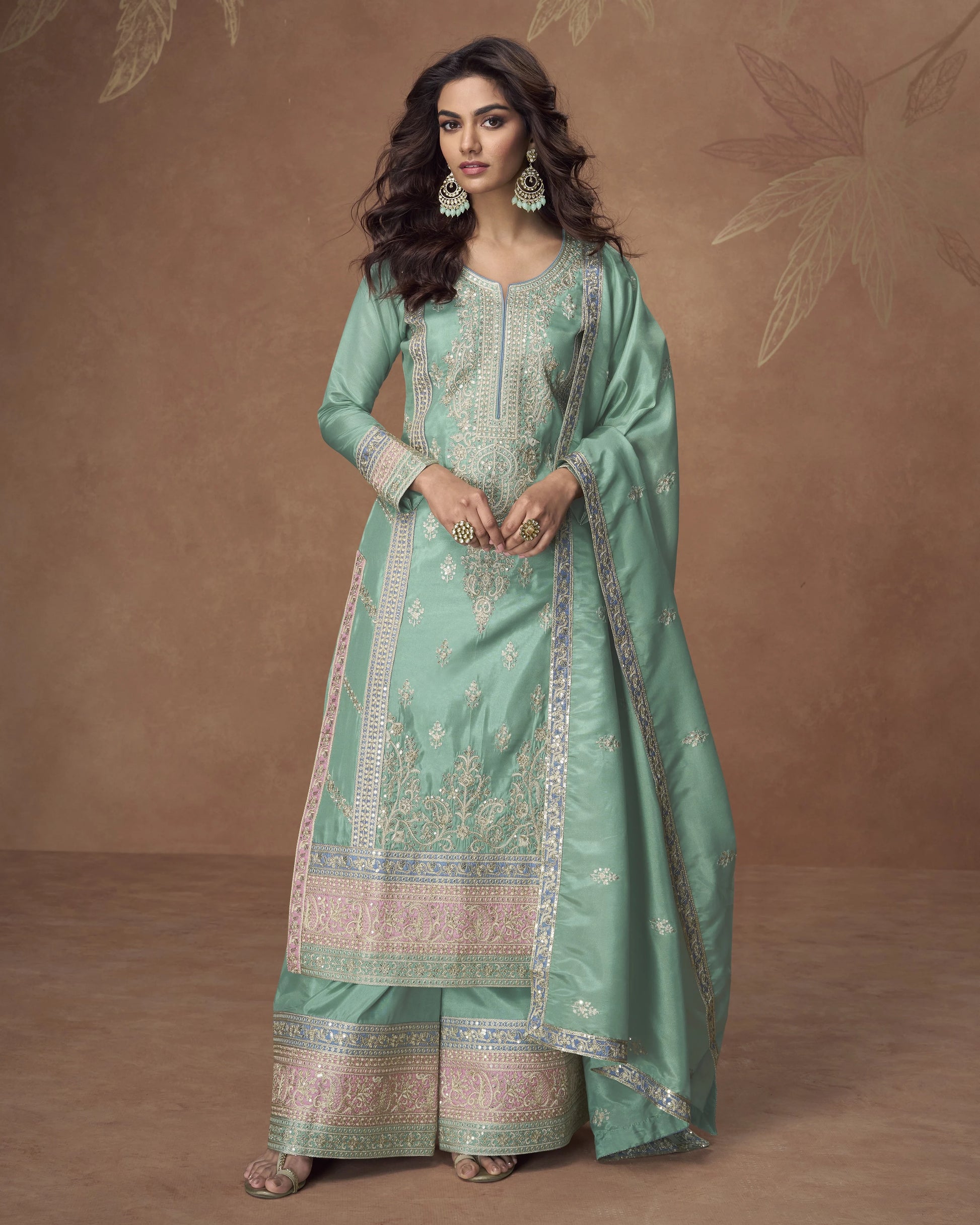 Woman wearing a traditional green outfit with intricate patterns against a brown background