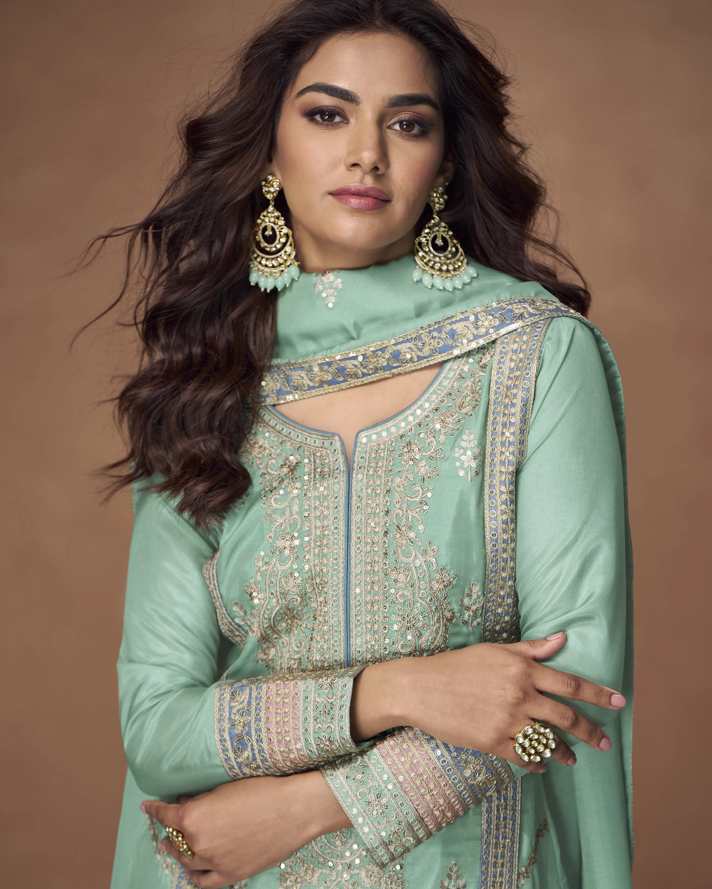 Woman wearing a light green traditional outfit with intricate patterns on a brown background