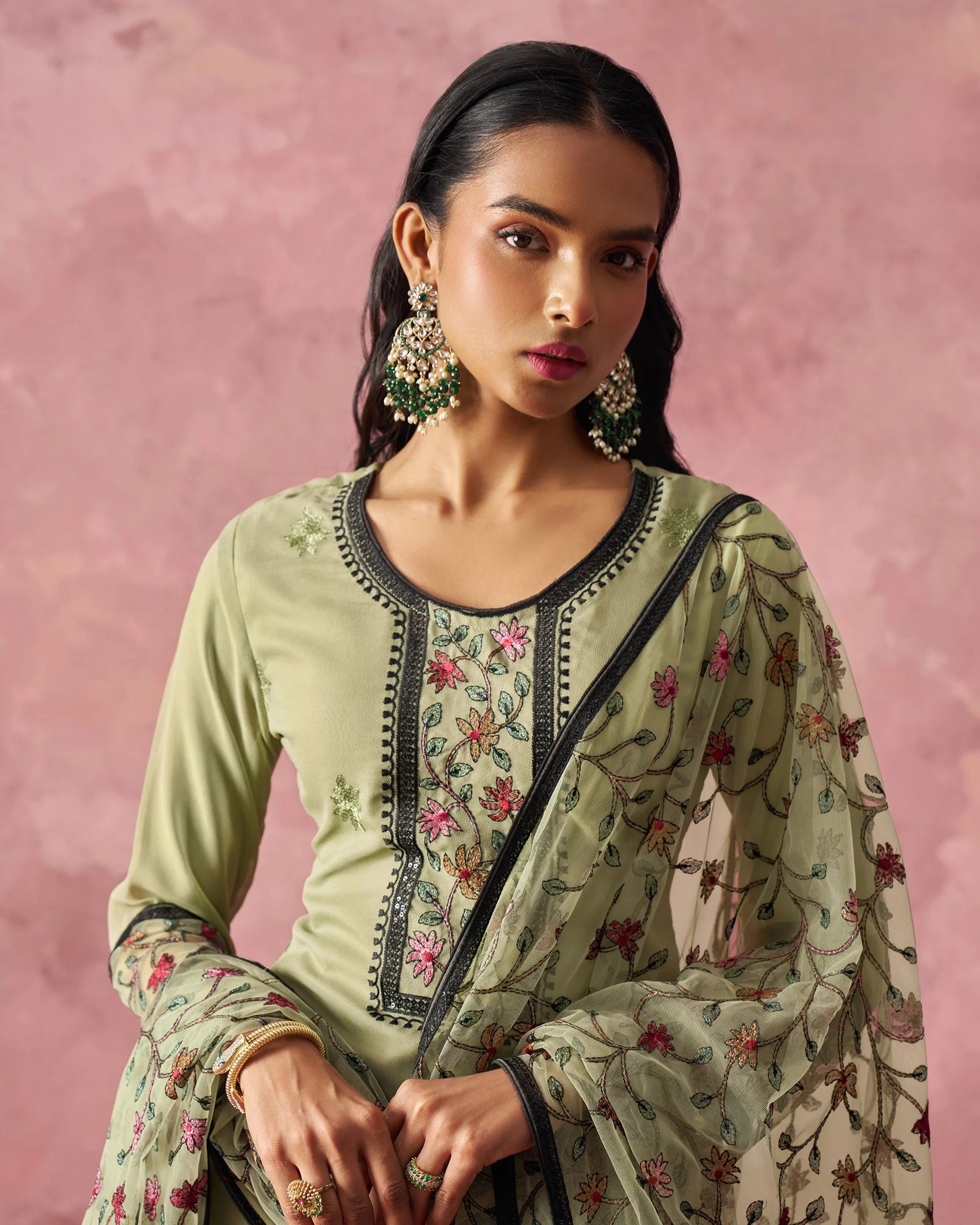 Woman wearing a light green embroidered outfit with a pink background