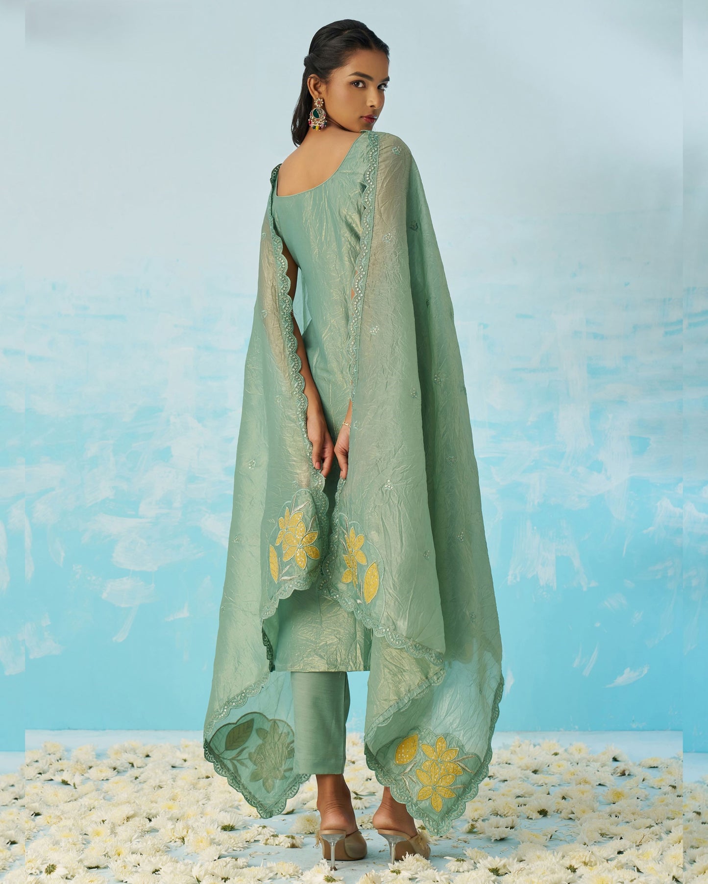 Woman wearing a light green traditional outfit with floral patterns against a blue background.