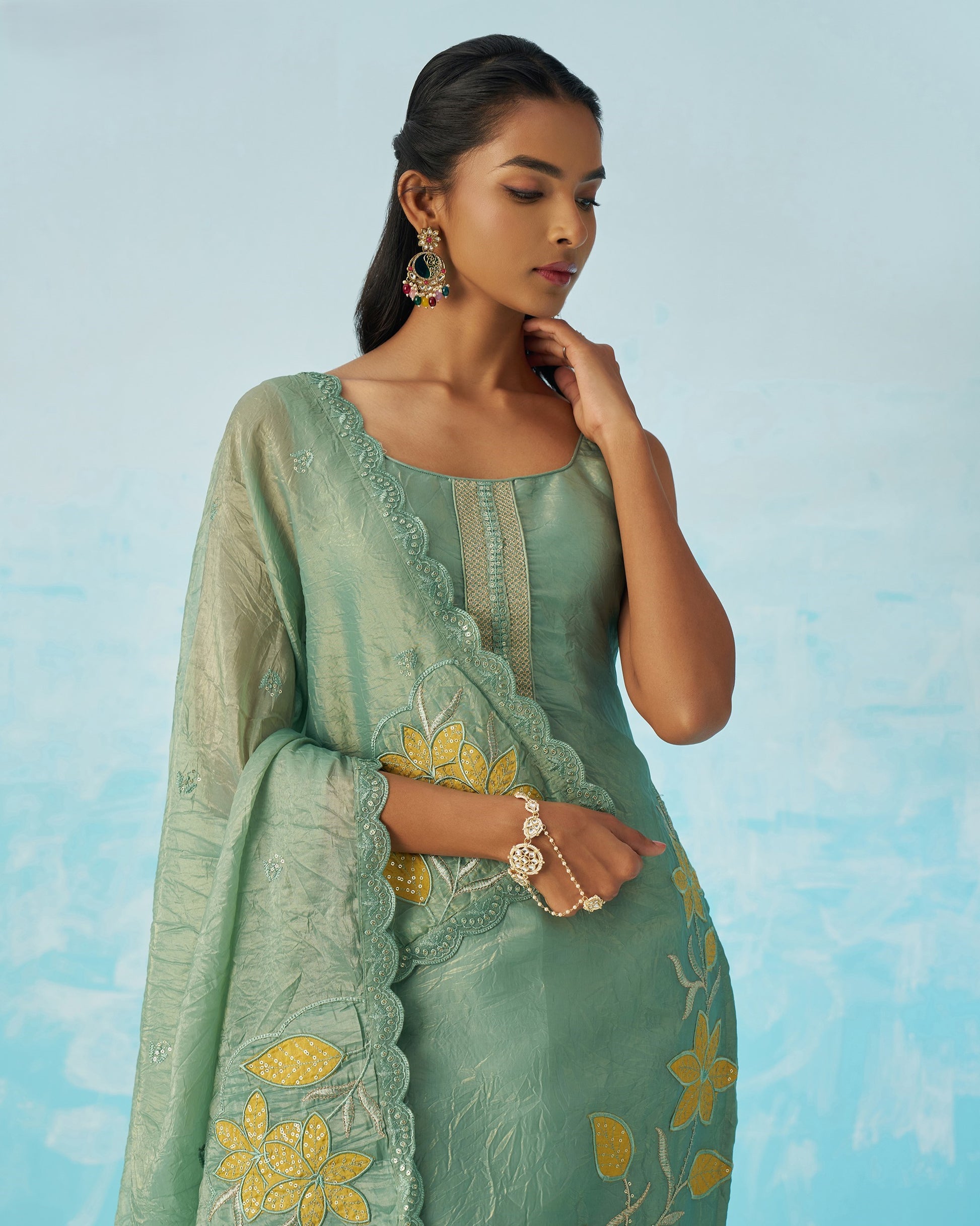 Woman wearing a light green embroidered traditional outfit against a blue sky background