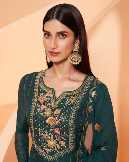 Woman wearing a green embroidered traditional outfit with gold detailing on a peach background