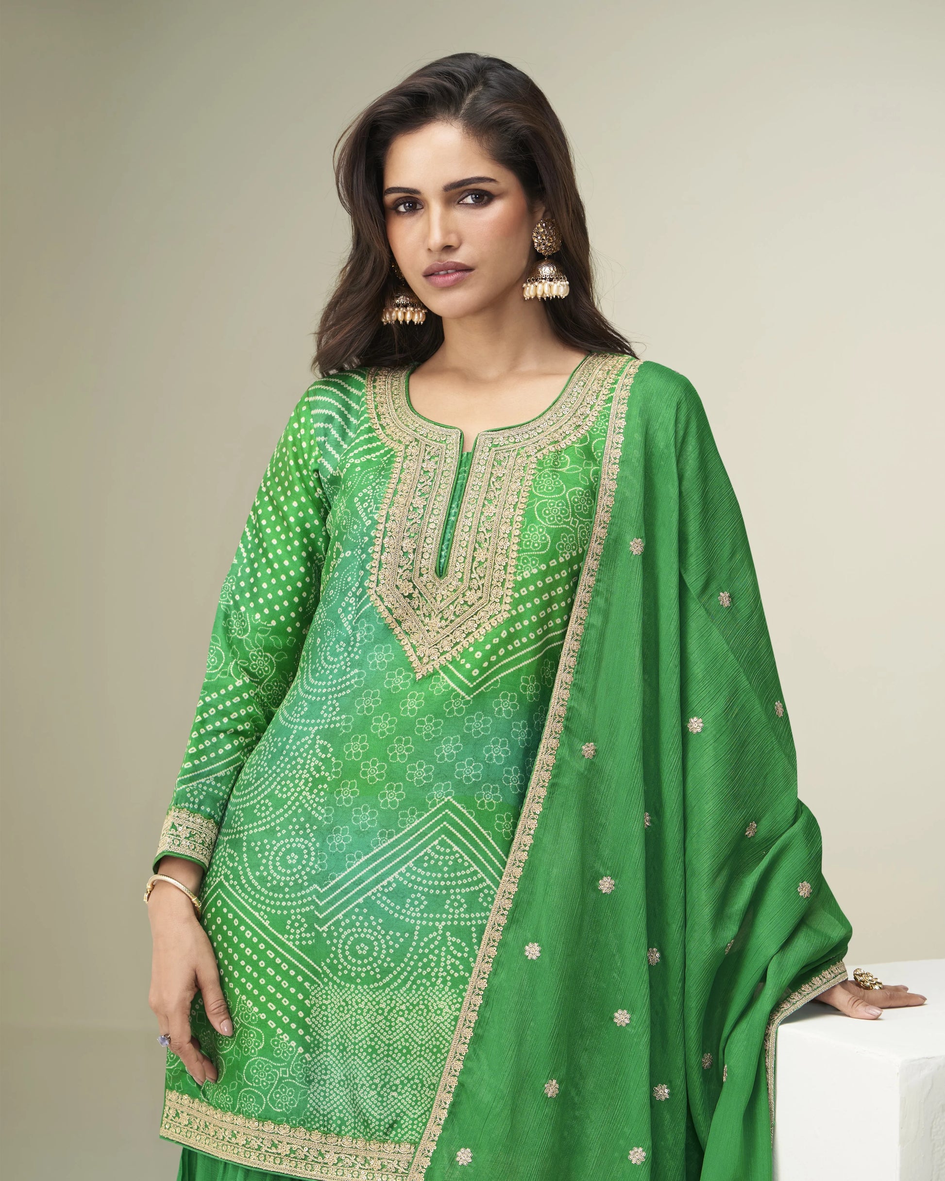 Woman wearing a green traditional outfit with intricate patterns on a plain background