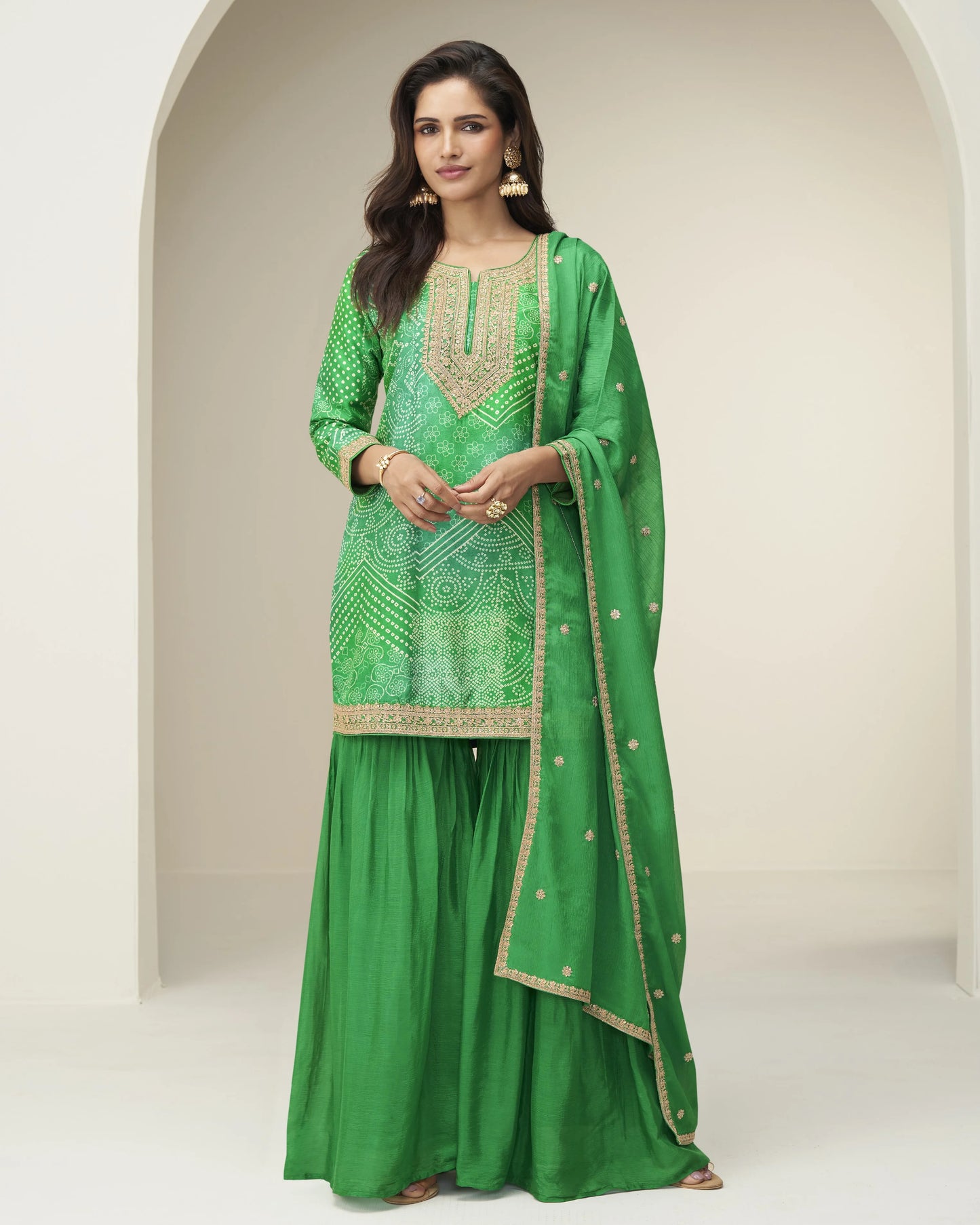 Woman wearing a green traditional outfit with gold embroidery in a neutral setting