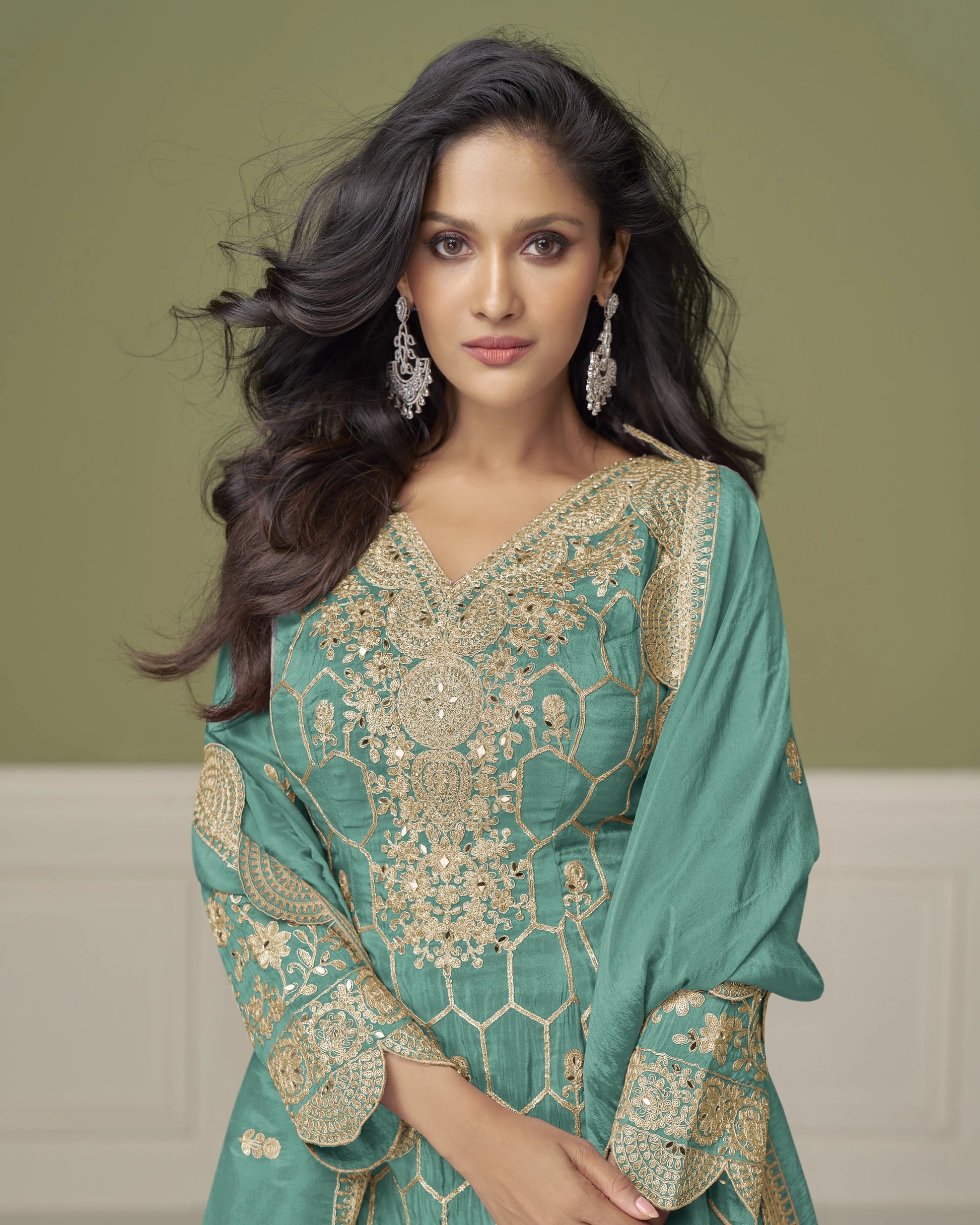 Woman wearing a green and gold embroidered traditional outfit against a beige background