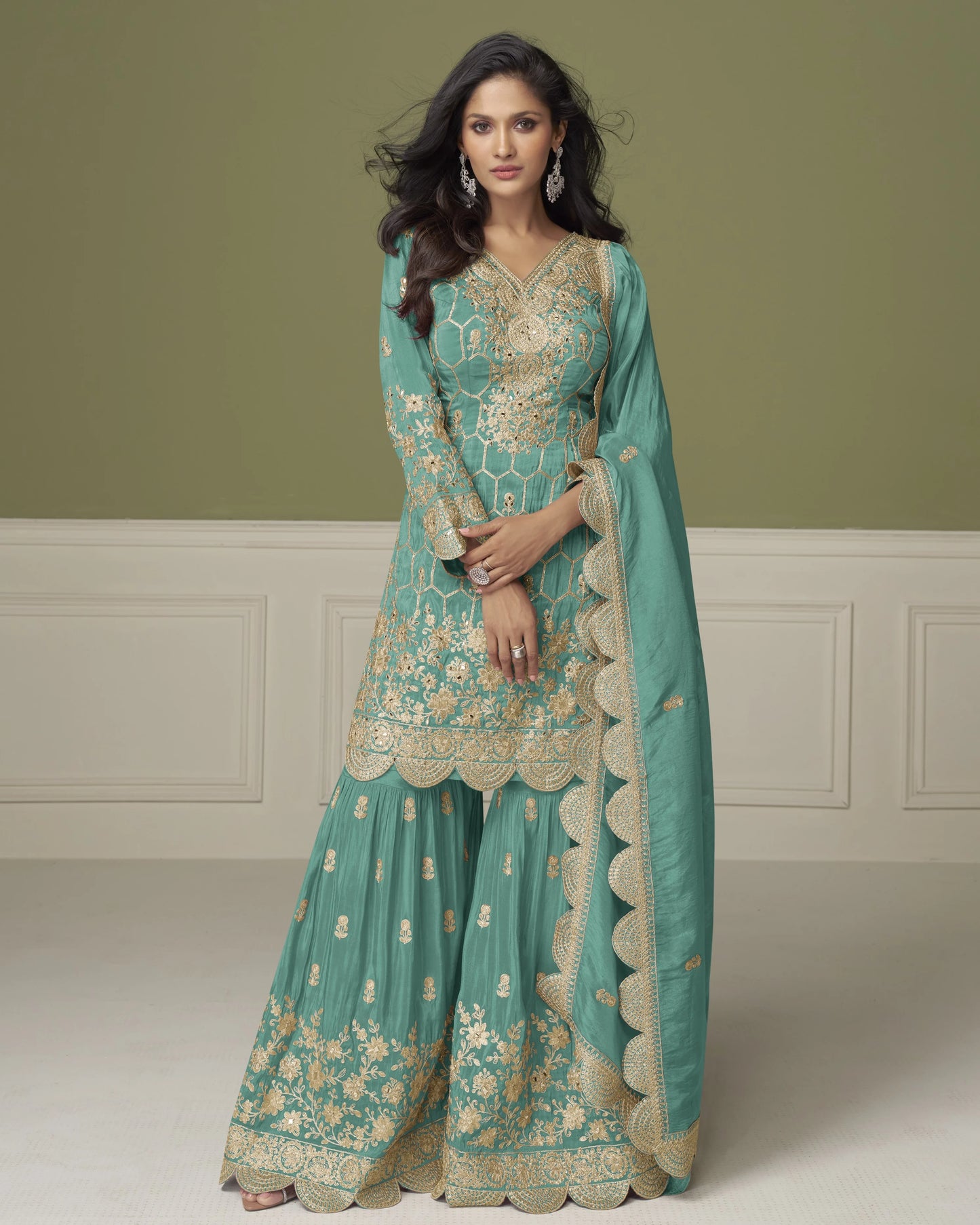 Woman wearing a teal embroidered traditional outfit with a matching dupatta against a neutral background