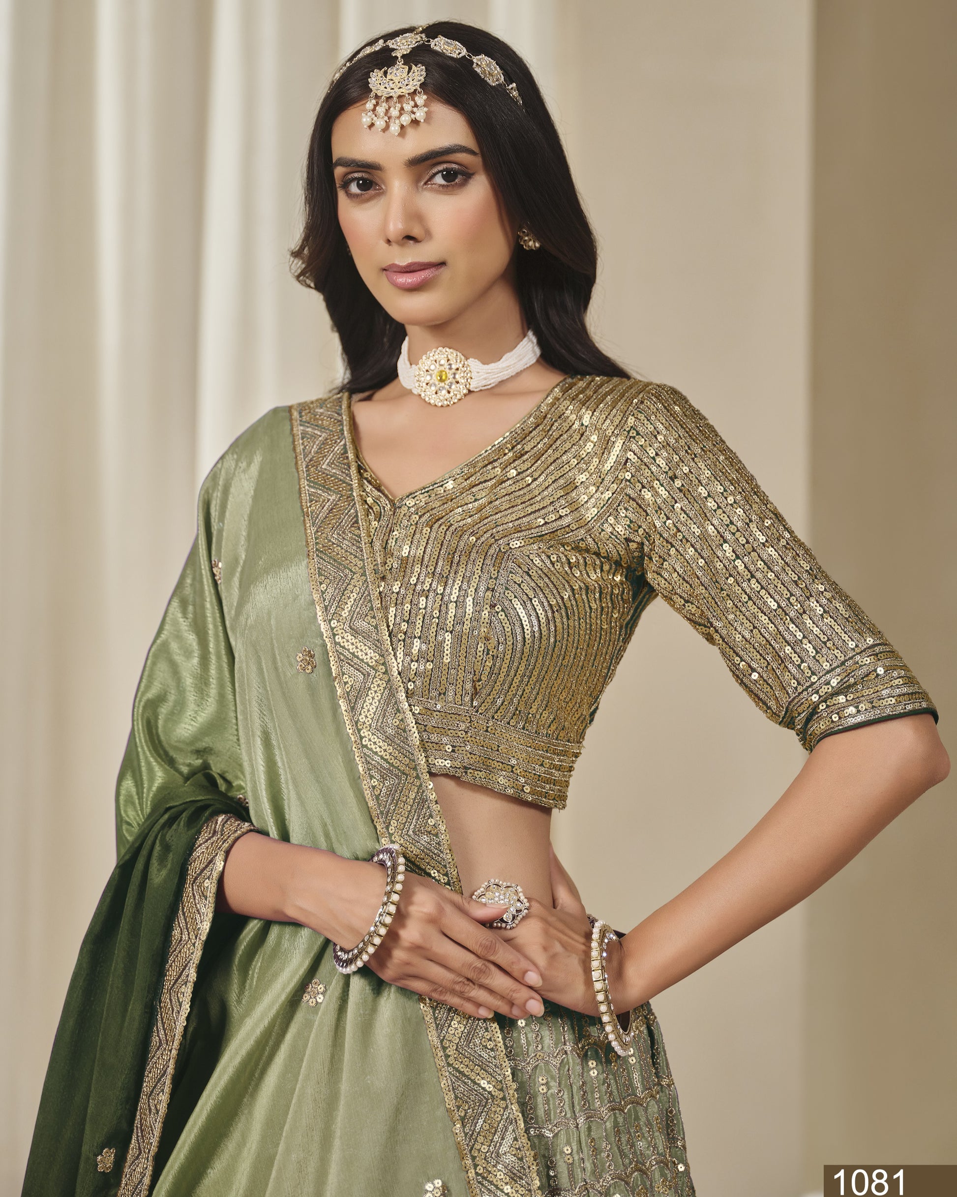 Woman wearing a green saree with gold blouse against a neutral background
