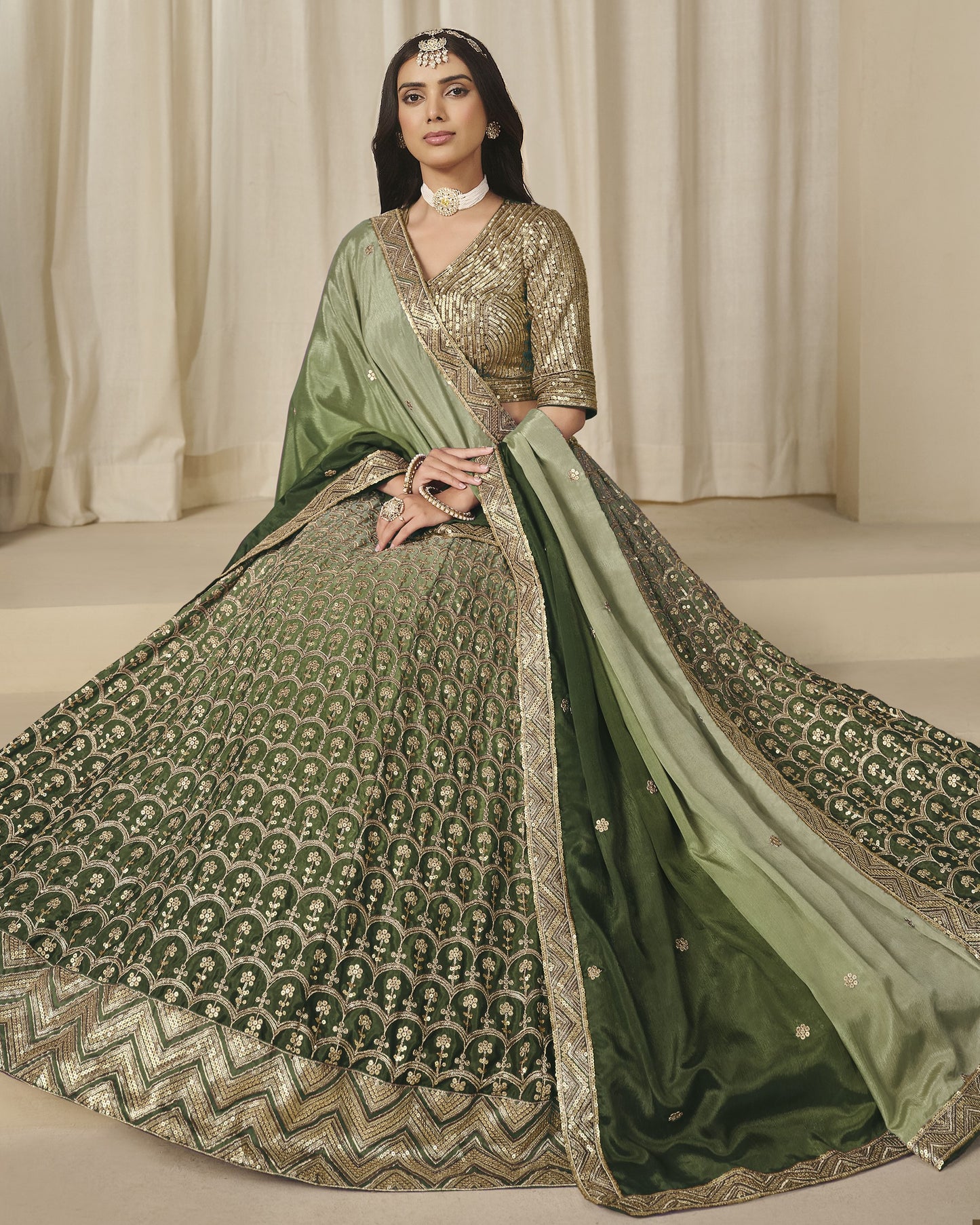 Woman wearing a green and gold traditional outfit with a matching dupatta against a neutral background