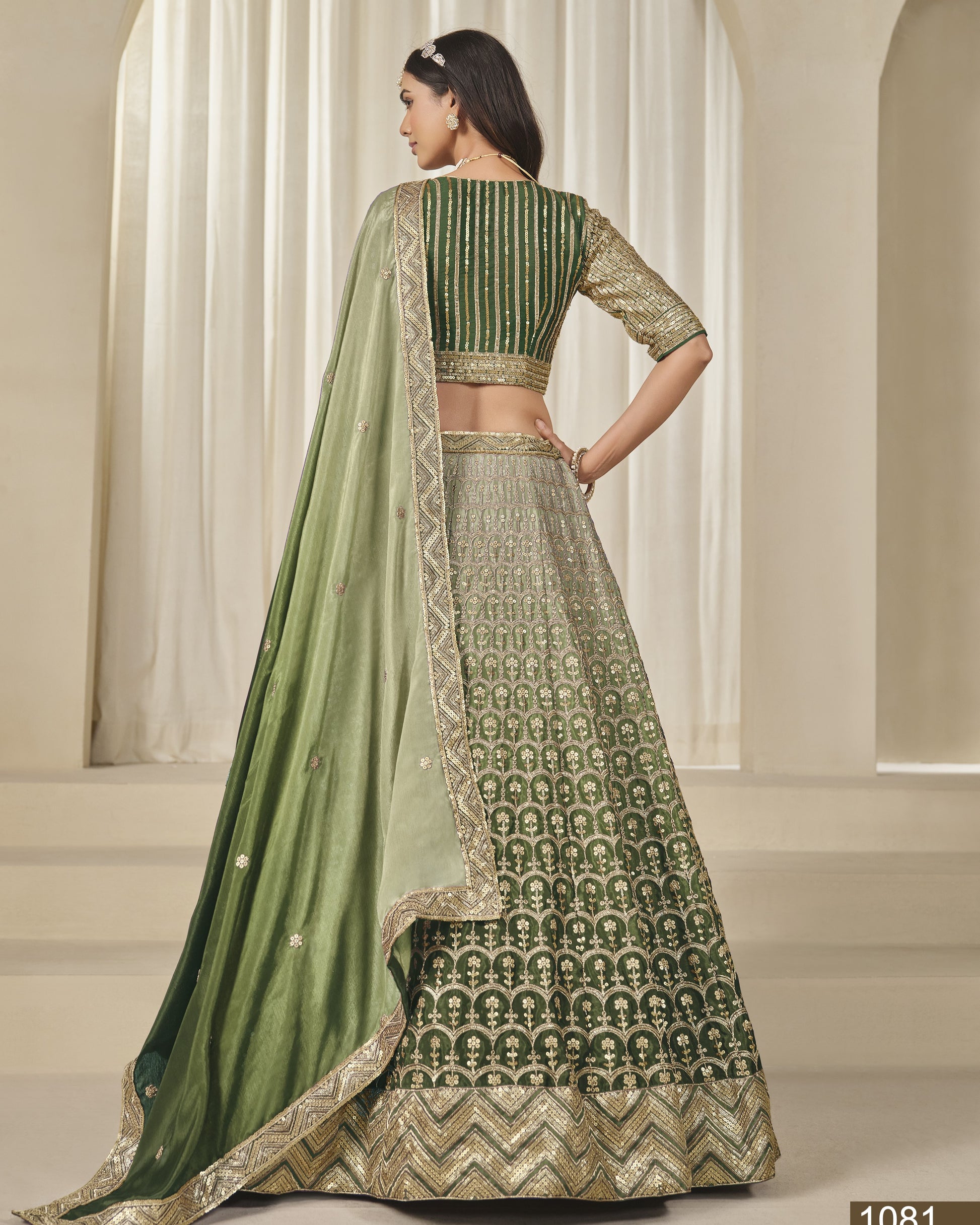 Woman wearing a green and gold traditional outfit with a patterned skirt in an indoor setting.