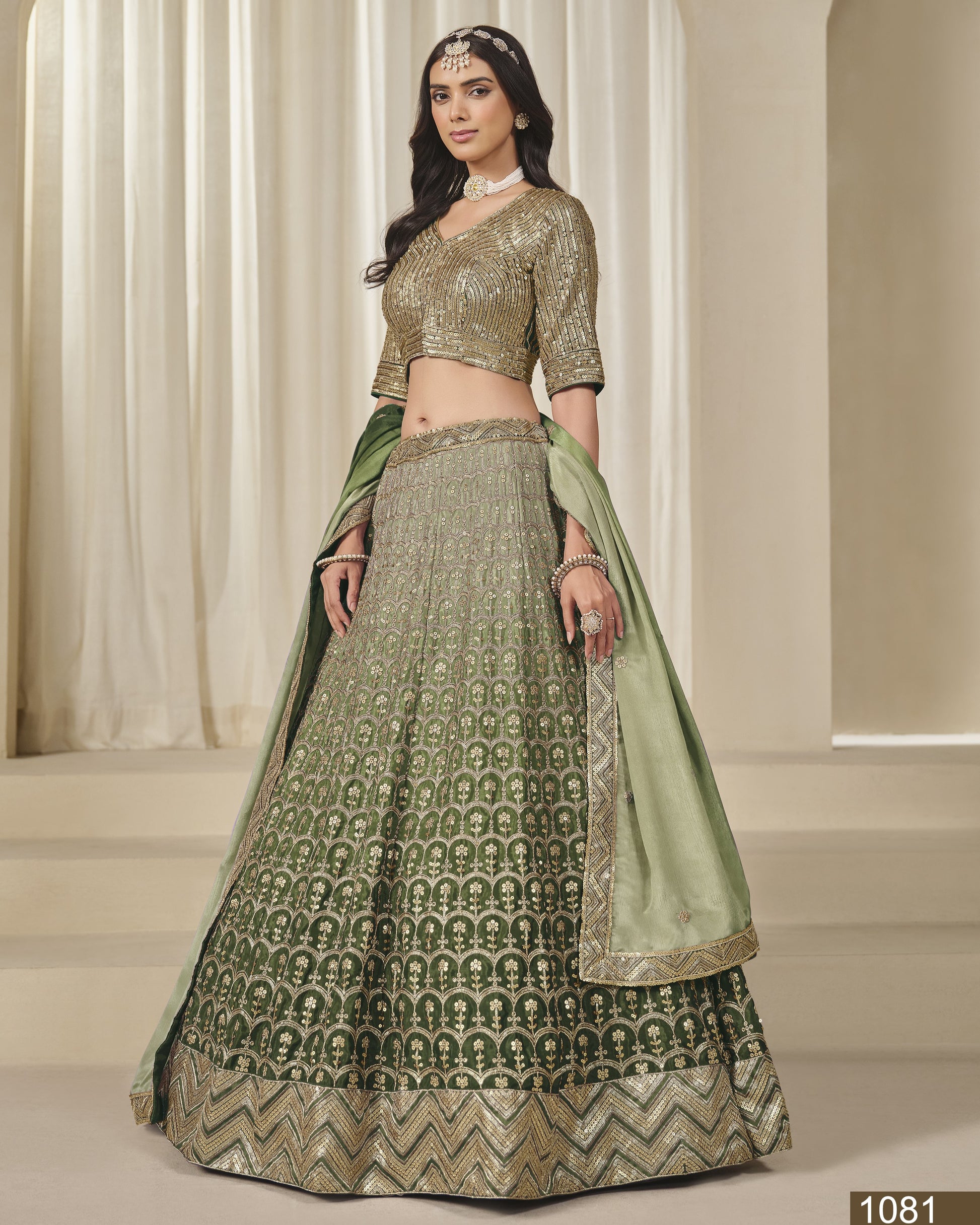 Woman wearing a green and gold traditional outfit with a matching dupatta in a neutral setting.