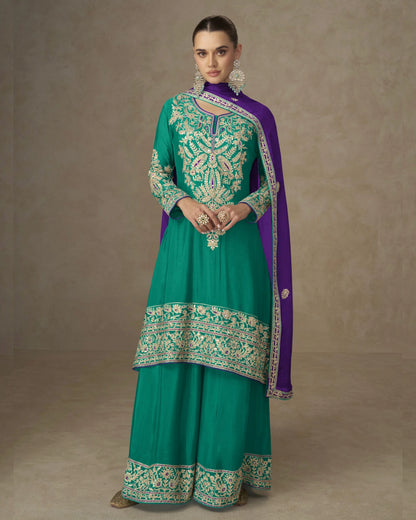 Woman wearing a teal and purple traditional outfit with intricate embroidery on a beige background