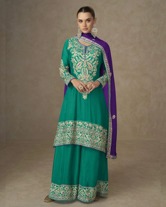 Woman wearing a teal and purple traditional outfit with intricate embroidery on a beige background