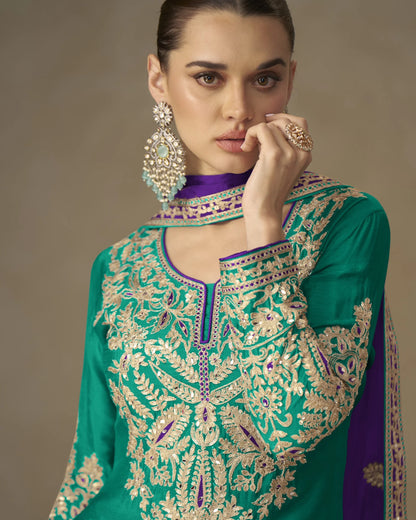 Woman wearing a green embroidered traditional outfit with jewelry against a neutral background
