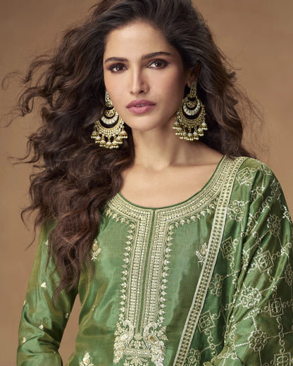 Woman wearing a green embroidered traditional outfit with gold jewelry against a brown background