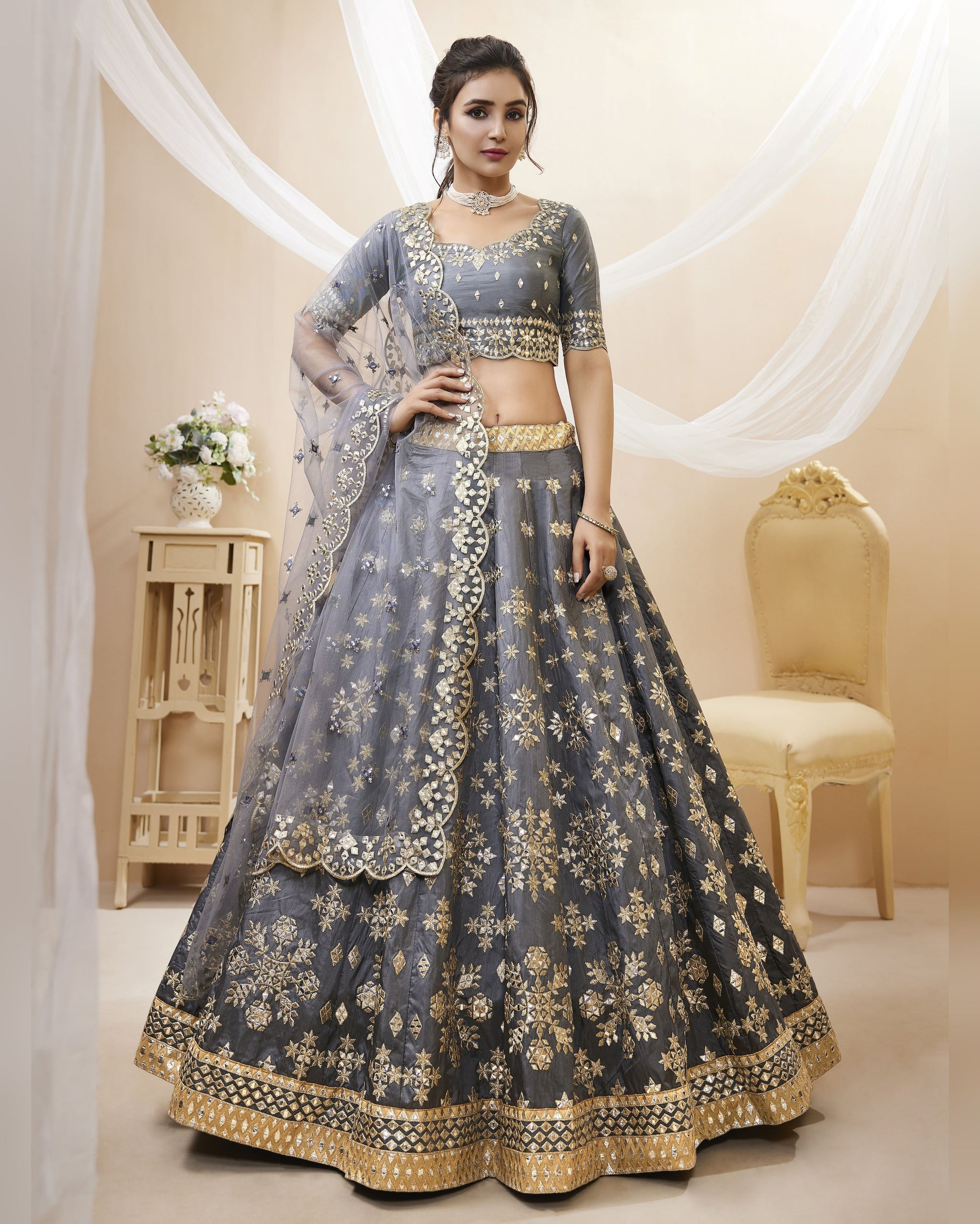 Woman wearing a gray and gold embroidered lehenga in a decorated room.