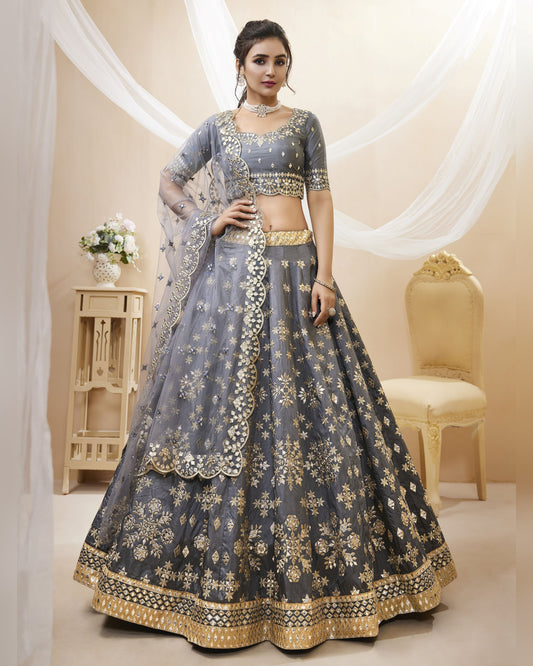 Woman wearing a gray and gold embroidered lehenga in a decorated room.