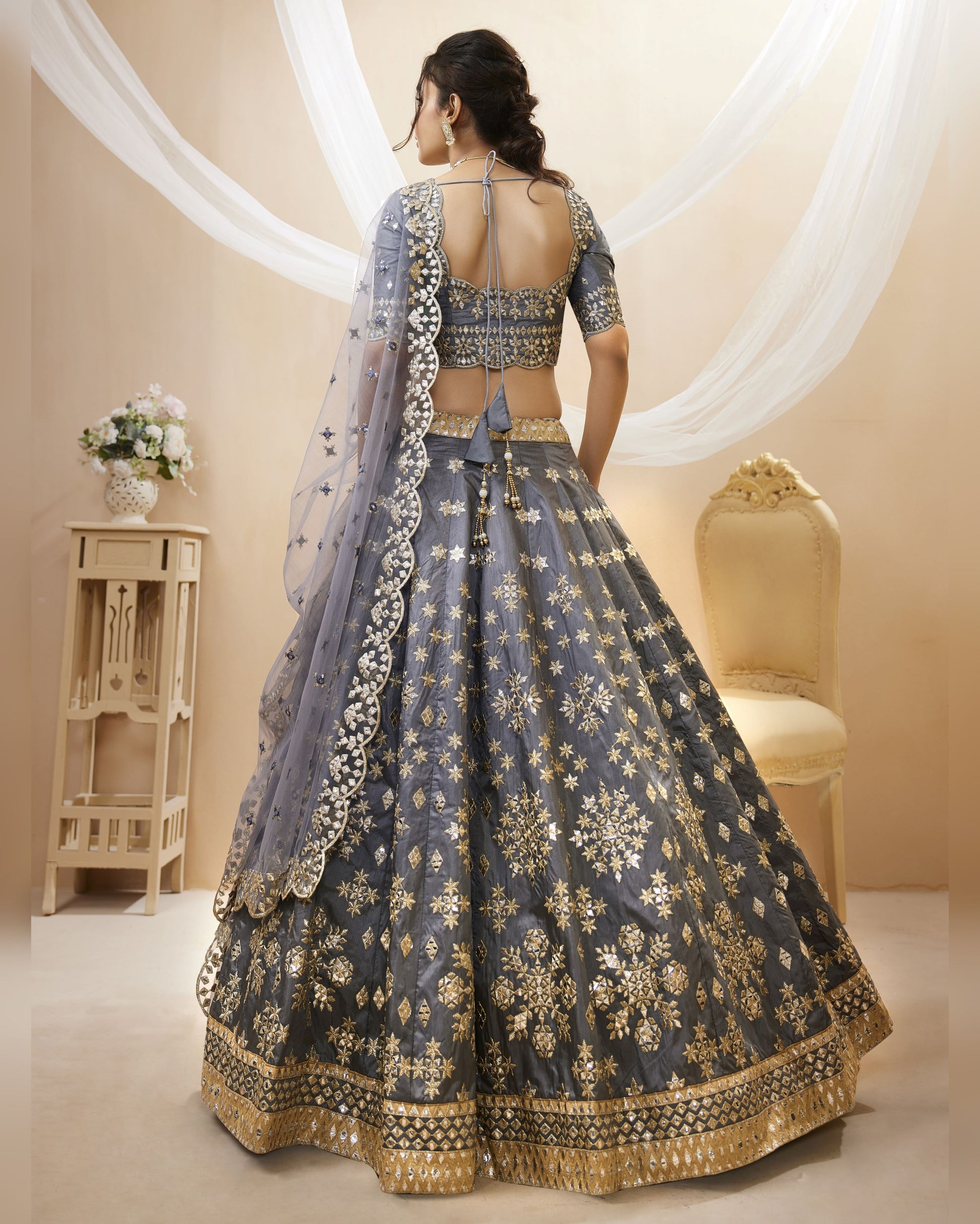 Woman wearing a traditional blue and gold embroidered lehenga in a decorated room.