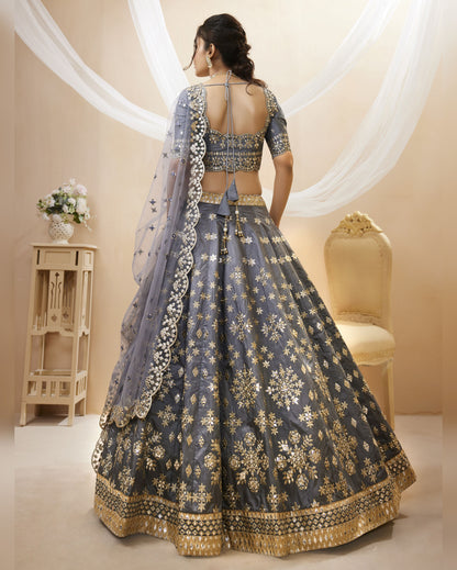 Woman wearing a traditional blue and gold embroidered lehenga in a decorated room.