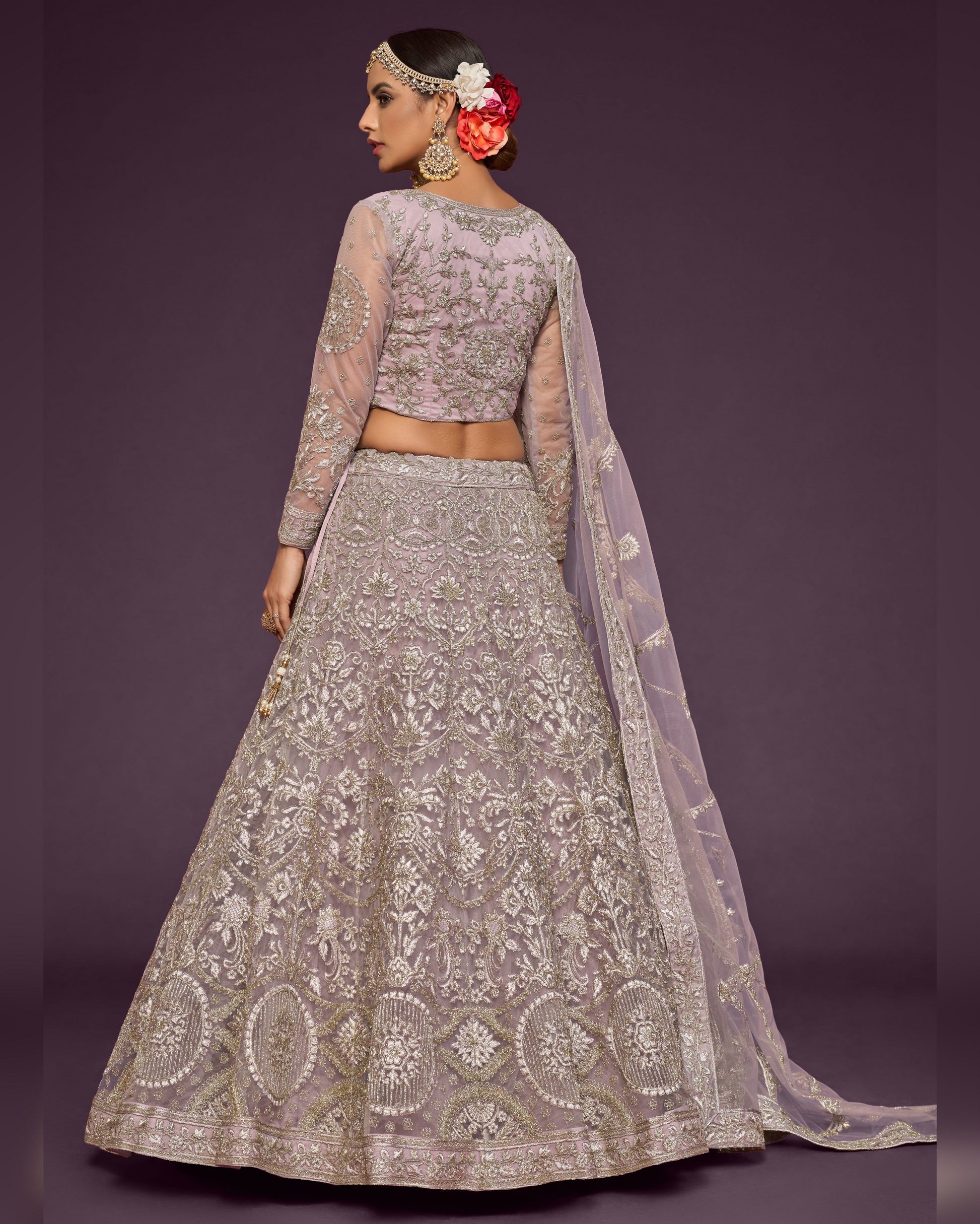 Woman wearing a silver embroidered lehenga with a matching blouse against a purple background