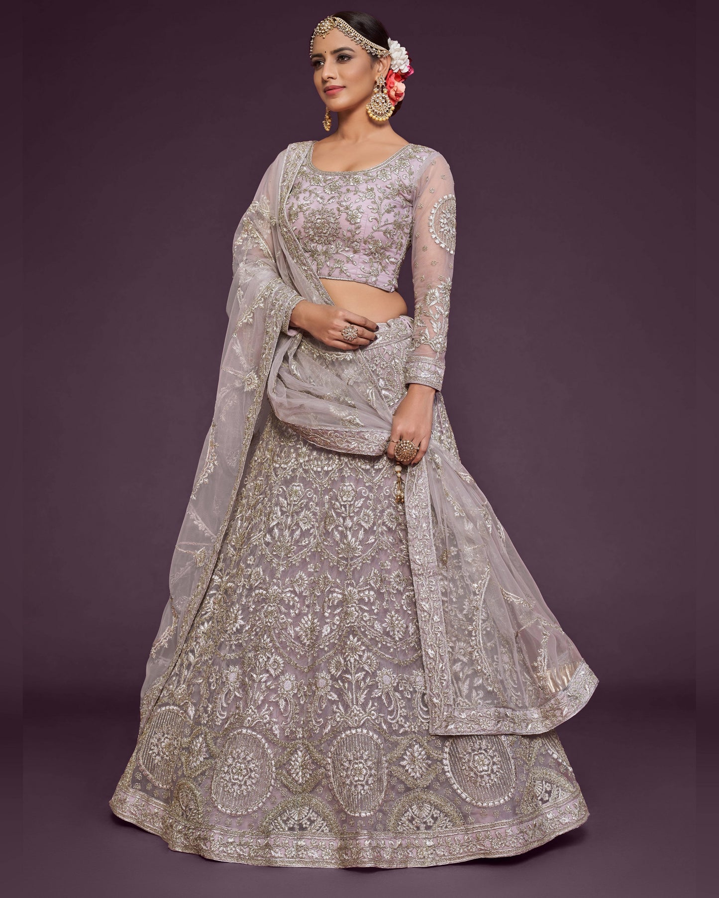 Woman wearing a silver embroidered lehenga with a matching blouse on a dark purple background