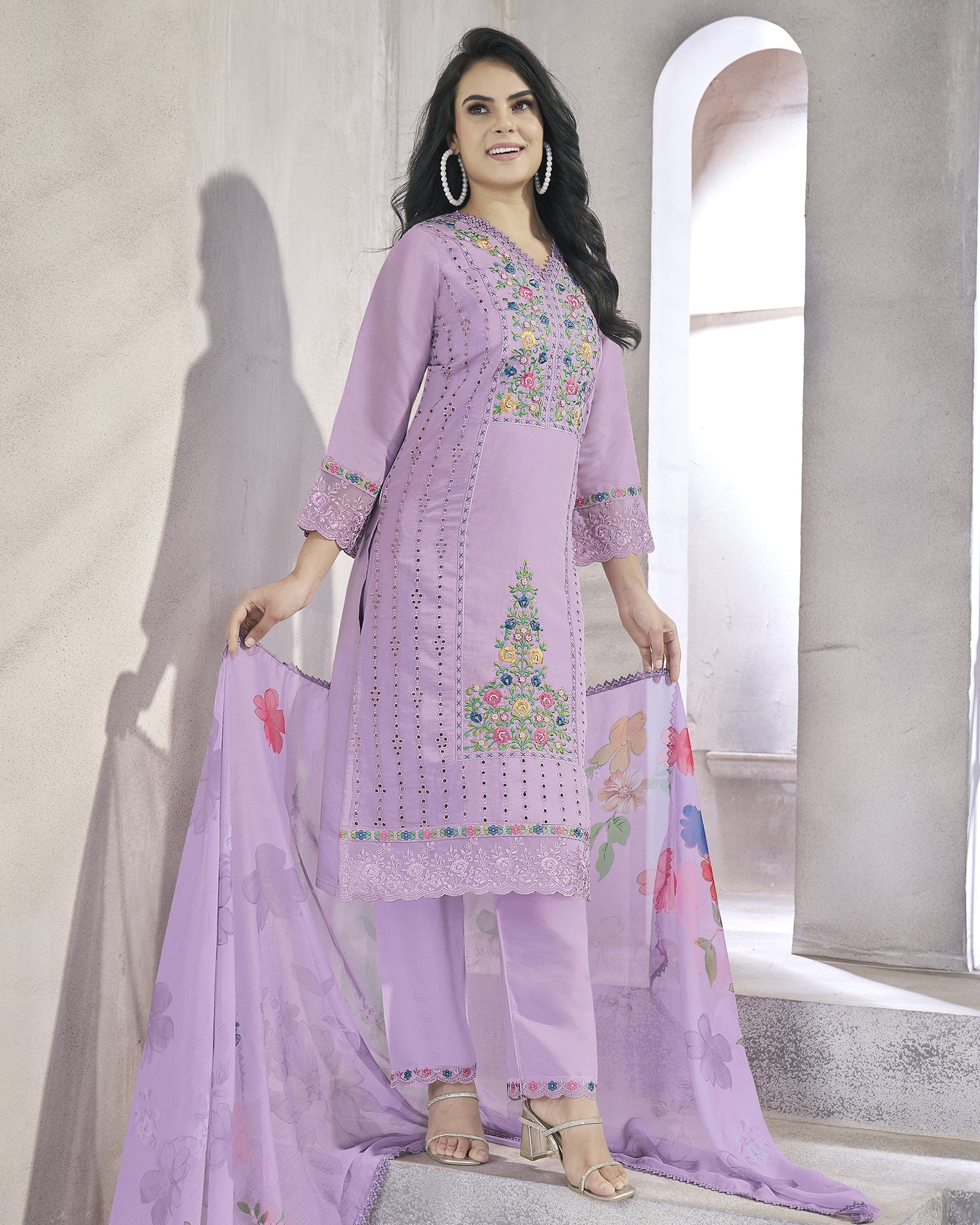 Woman wearing a light purple embroidered outfit with a floral dupatta in a neutral setting.