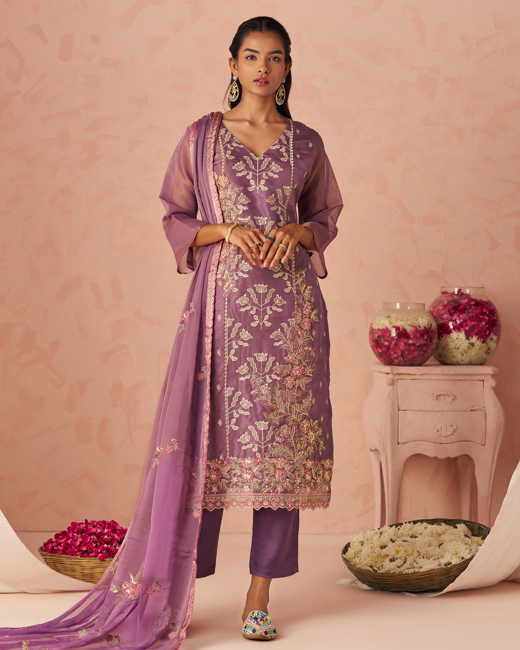 Woman wearing a purple embroidered outfit with a pink background